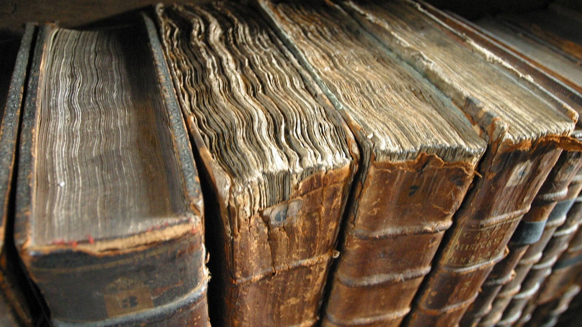 中世紀 桌布 壁紙 — 古老皮革裝訂書籍的特寫，書脊磨損，書頁風化，展現了數世紀的使用痕跡。