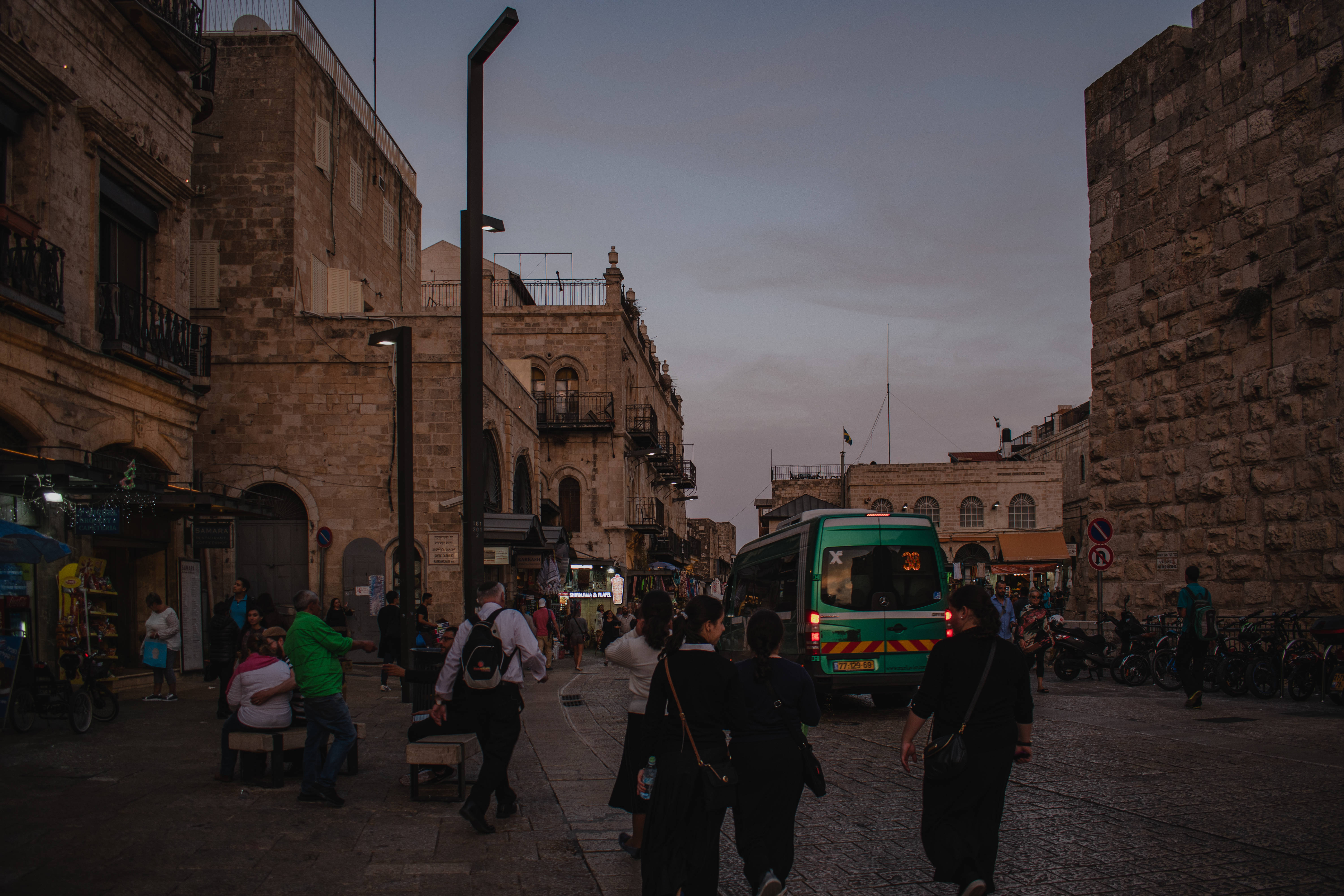 Israel 桌布 壁紙 — 古老石城中的繁華暮色街道，行人與一輛綠色巴士經過。
