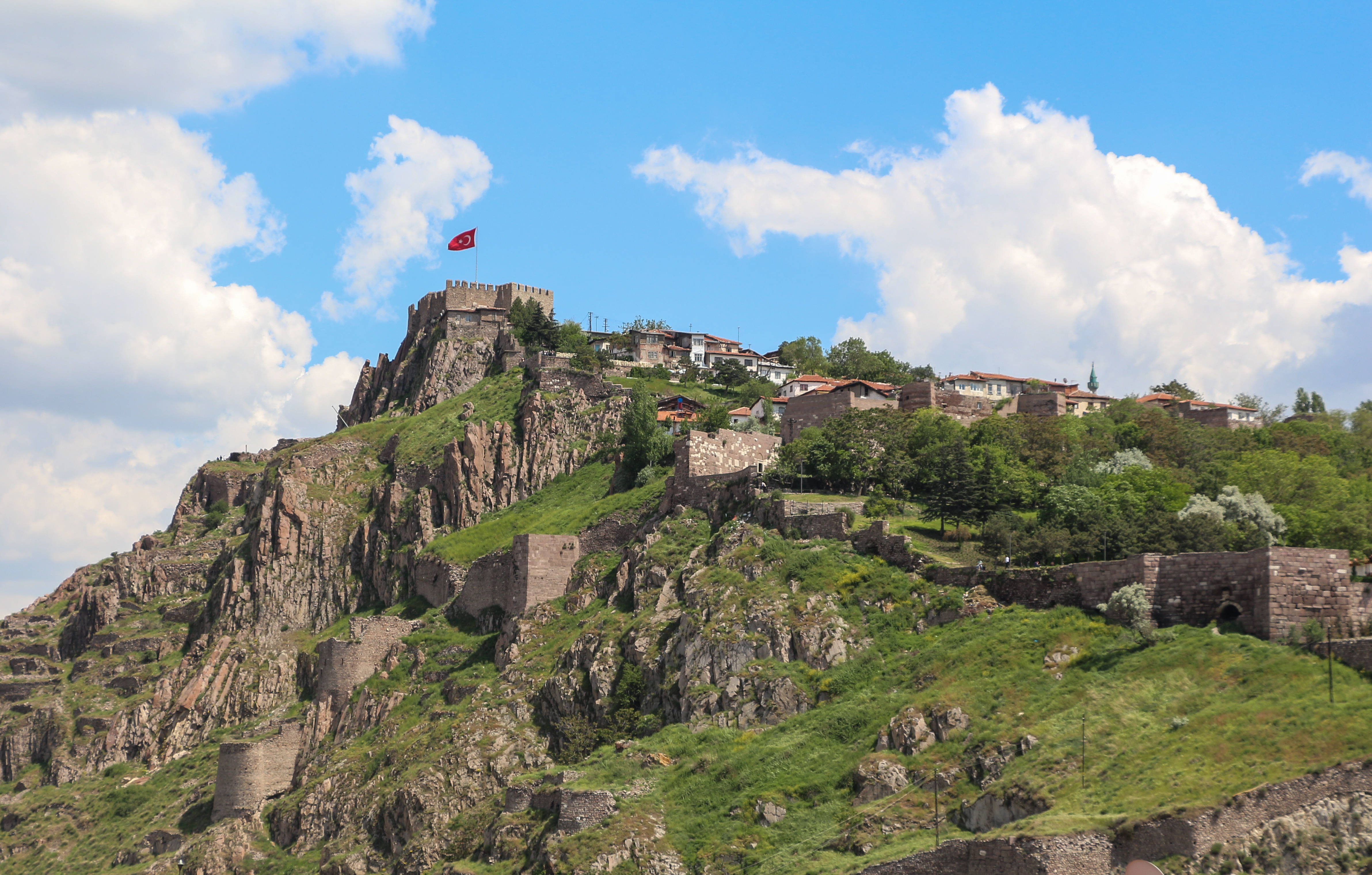 Ankara 桌布 壁紙 — 古老石堡矗立在崎嶇的綠色山丘上，藍天白雲，紅旗飄揚。