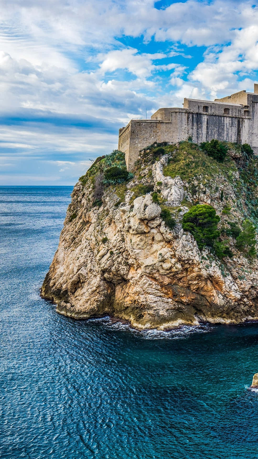 wall 桌布 壁紙 — 古老石堡聳立在崎嶇懸崖上，俯瞰深藍色大海，天空局部多雲。