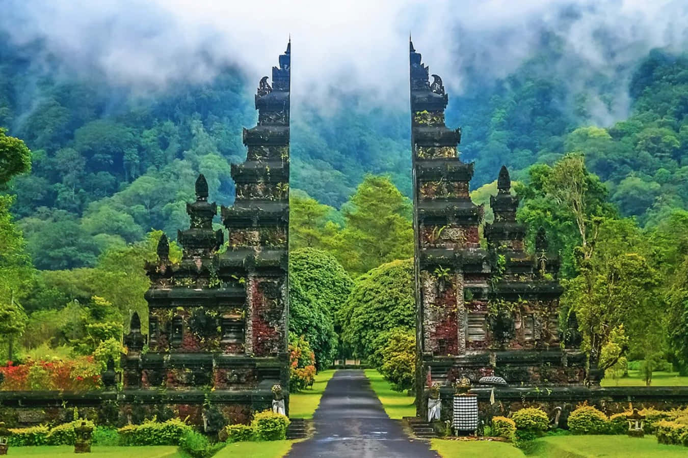 印尼 桌布 壁紙 — 古老石廟大門聳立在茂密翠綠的叢林中，背景是霧氣繚繞的山巒。