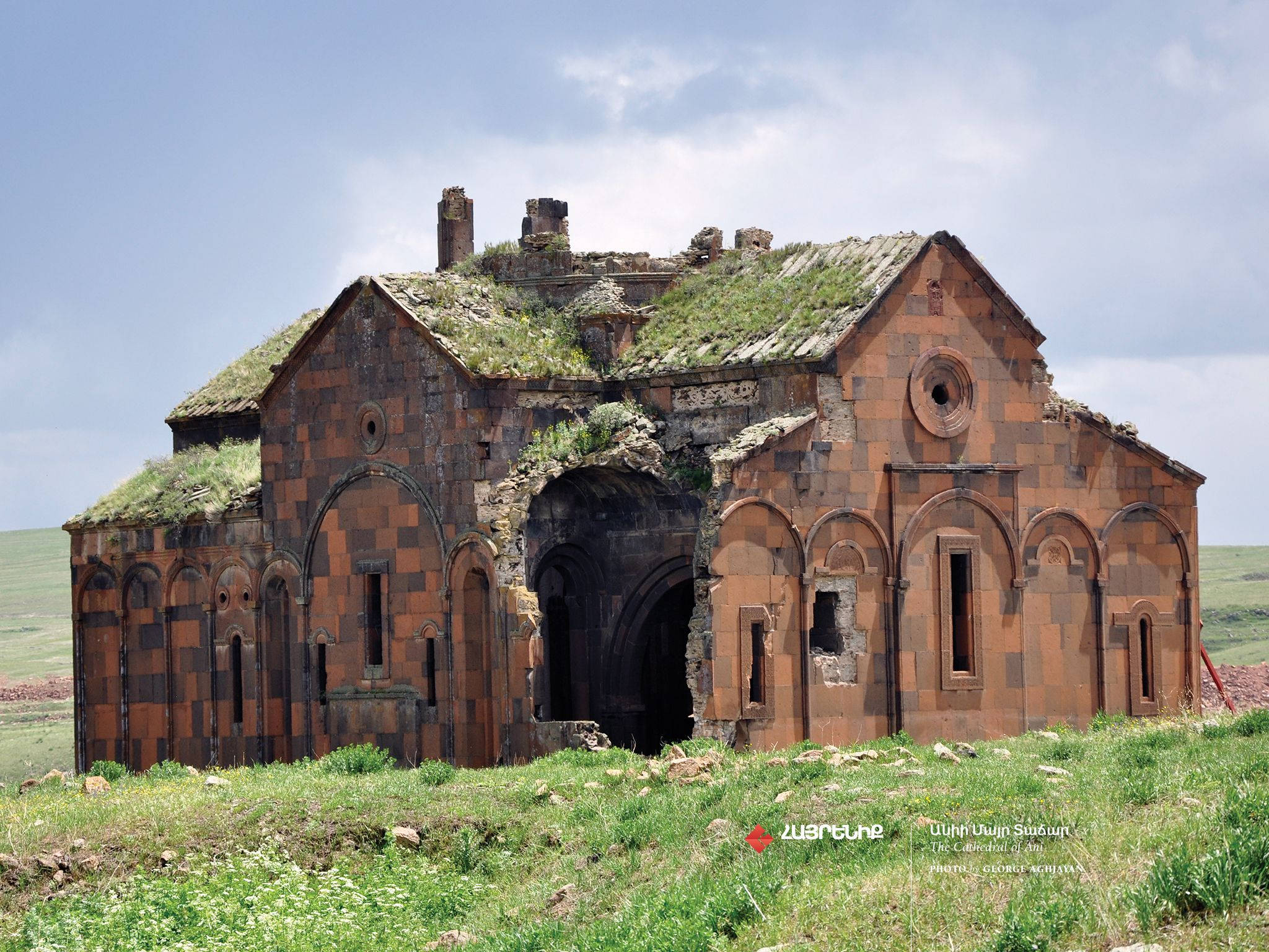 Armenia 桌布 壁紙 — 古老石教堂遺址，屋頂長滿苔蘚，莊嚴地矗立在草地上，天空部分多雲。