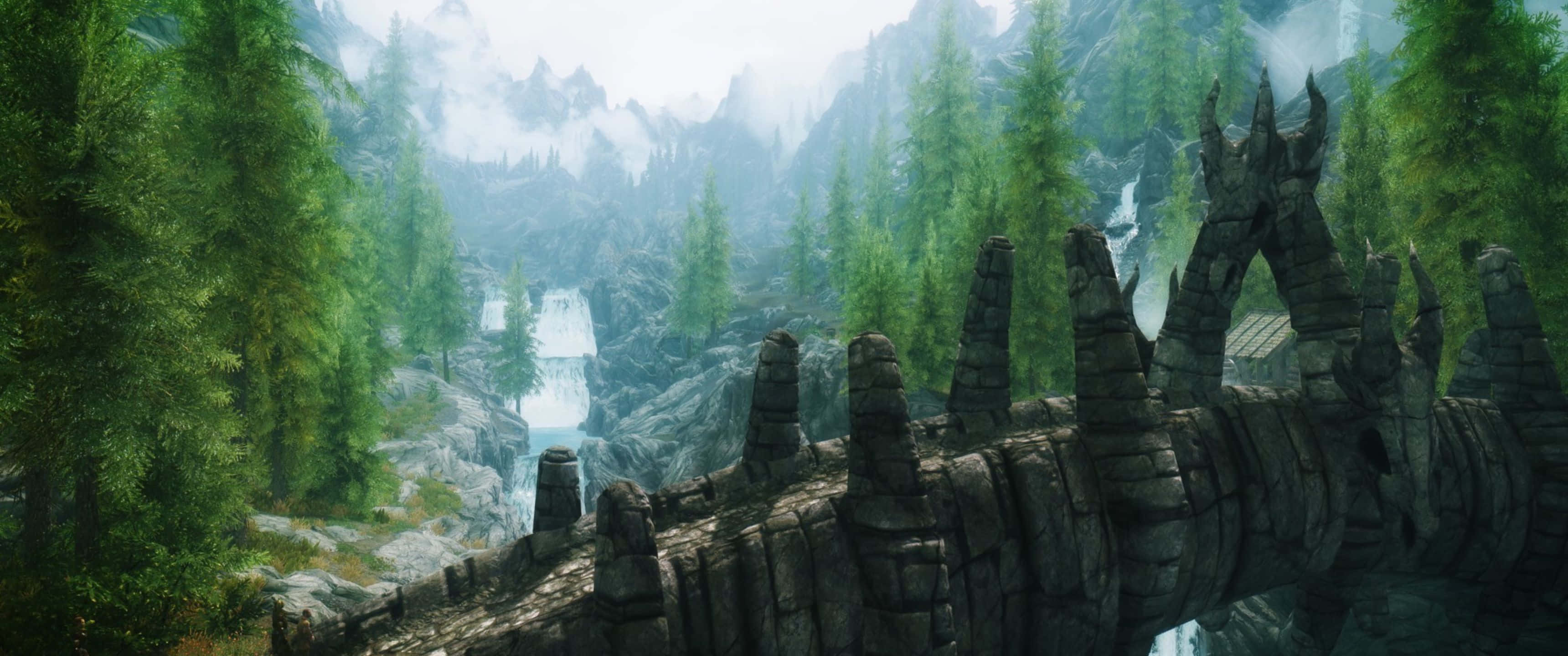 3440x1440p The Elder Scrolls V Skyrim 桌布 壁紙 — 古老石橋帶尖塔橫跨霧氣瀰漫的山谷，兩側是茂密的常綠森林和層疊瀑布。