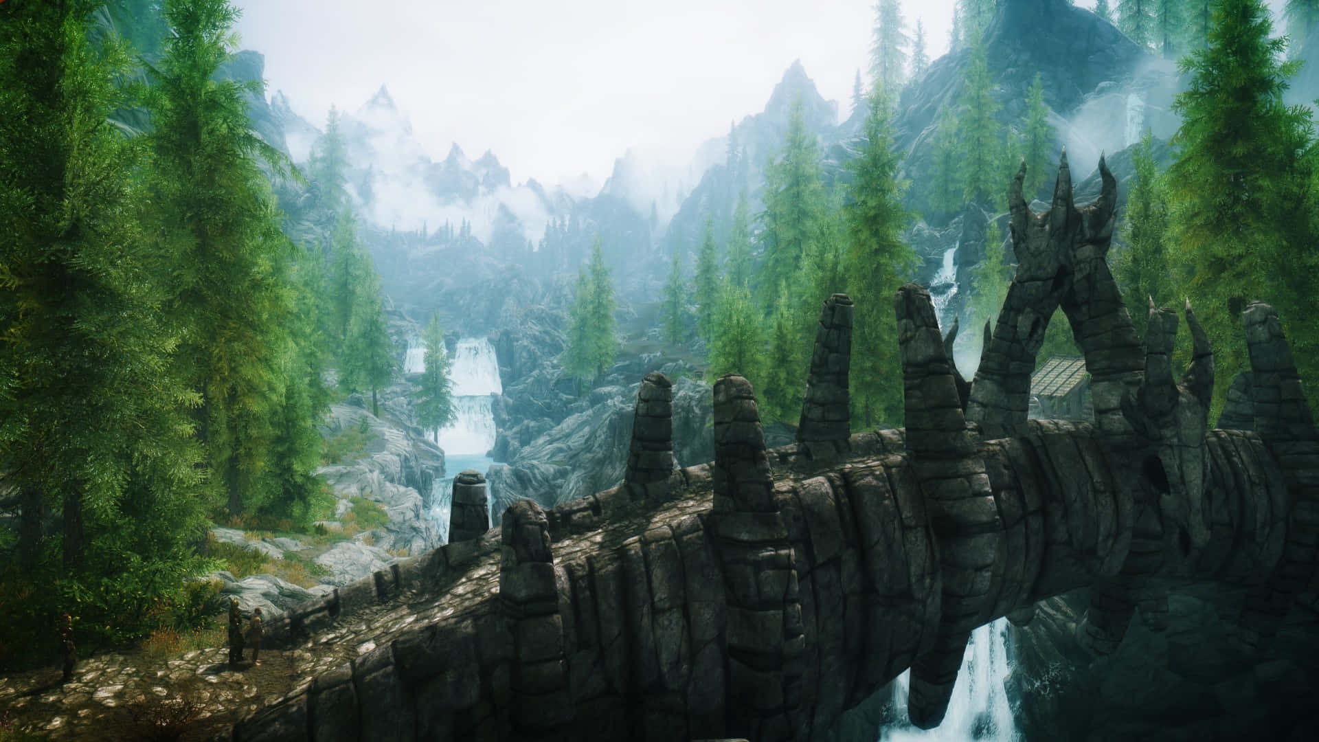 Skyrim Landscapes 桌布 壁紙 — 古老石橋帶鋸齒狀尖塔橫跨霧氣瀰漫的河流，穿過茂密的松林，遠處有積雪覆蓋的山峰。