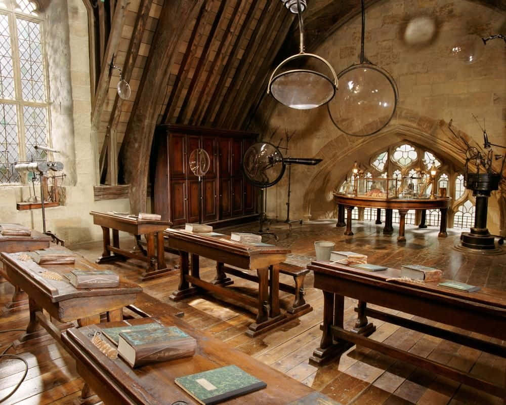 The Hogwarts Potions Class 桌布 壁紙 — 古老石牆教室，內有木製書桌、書籍和拱形窗戶下漂浮的玻璃球體。