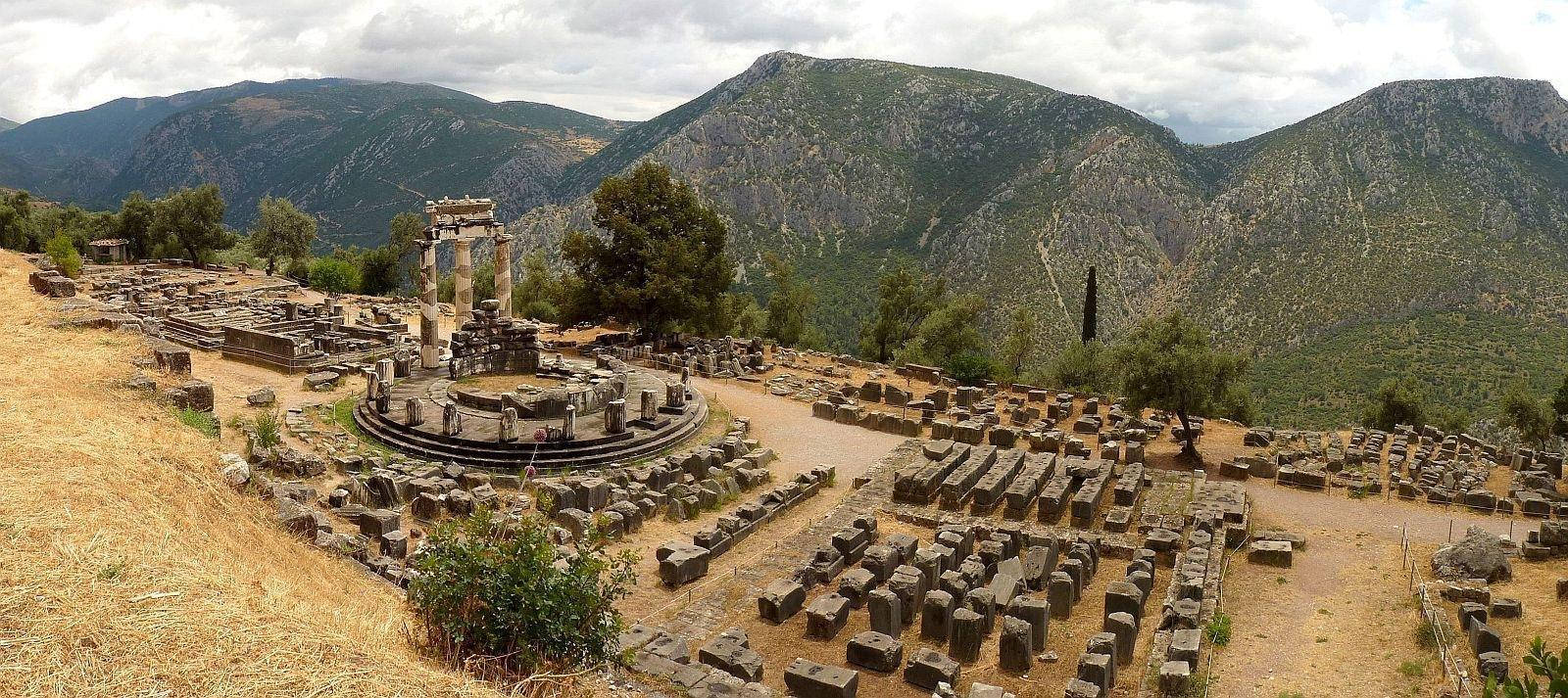 Holy 桌布 壁紙 — 古老石頭廢墟，一個圓形寺廟建築群，坐落於乾燥山谷中，被綠山環繞，天空多雲。