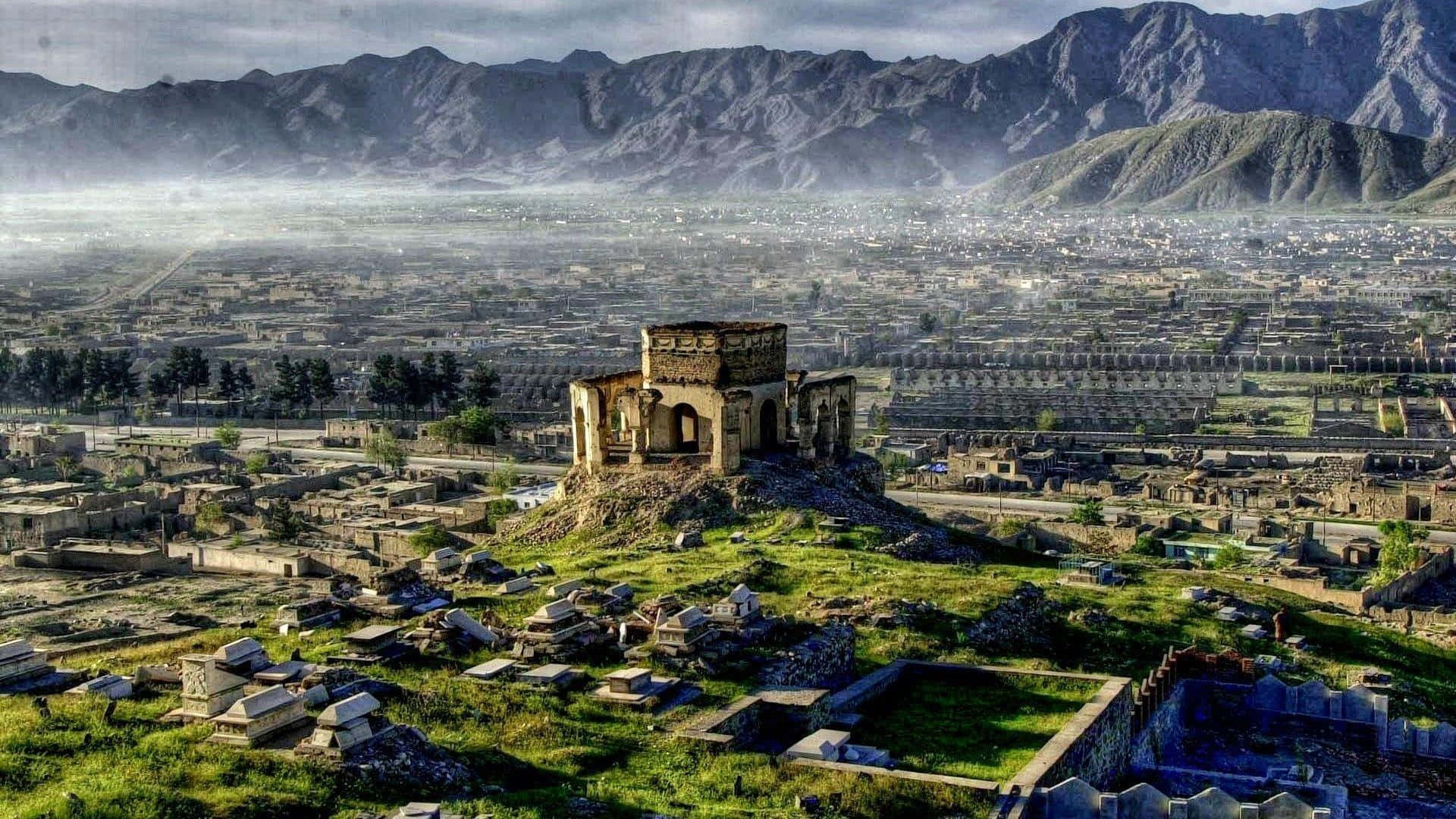 Afghanistan 桌布 壁紙 — 古老石頭廢墟位於長滿青草的山丘頂部，俯瞰著坐落在霧氣繚繞的山谷中的廣闊城市。