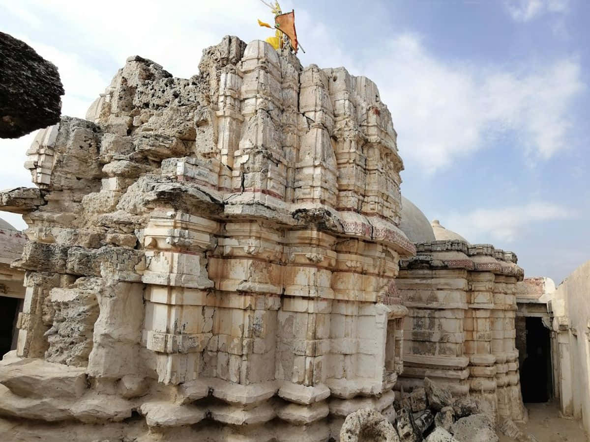 Hindu Temple 桌布 壁紙 — 古老風化的石廟遺跡，帶有精緻雕刻，矗立在明亮的藍天下，散落著幾朵雲。