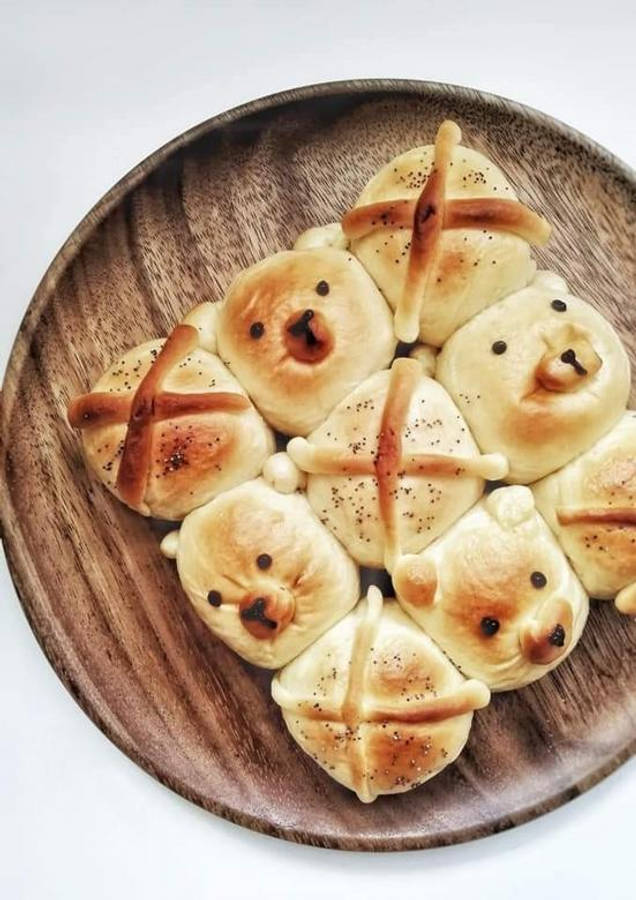 Pastries 桌布 壁紙 — 可愛的熊仔形狀十字包，金黃色外皮，罌粟籽點綴，擺放在質樸的木盤上。
