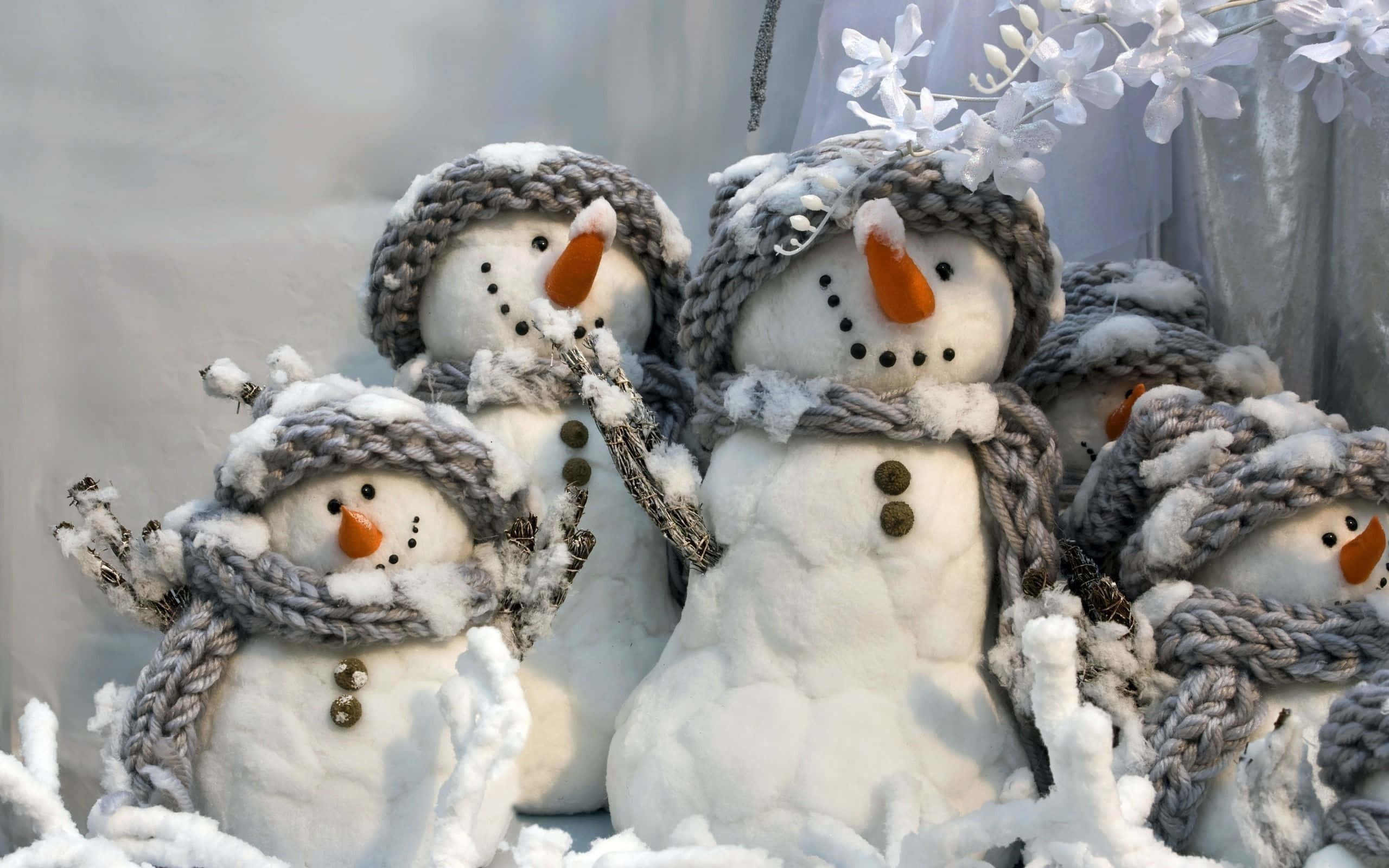 Winter Scene 桌布 壁紙 — 可愛的雪人戴著針織帽和圍巾，站在白雪皚皚的冬日場景中，帶有白色花卉點綴。