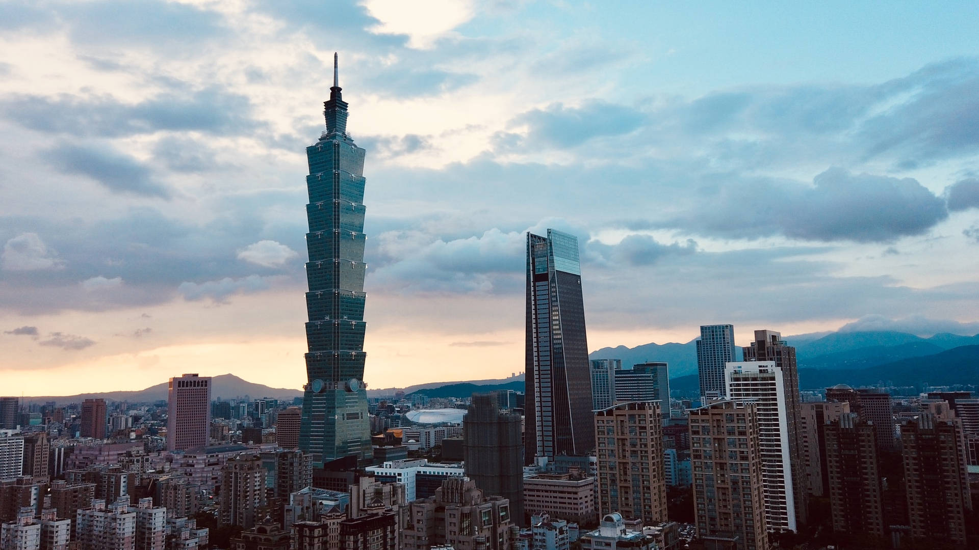 台北101大樓在日落時分，背後襯著山巒，聳立在密集的城市之上。