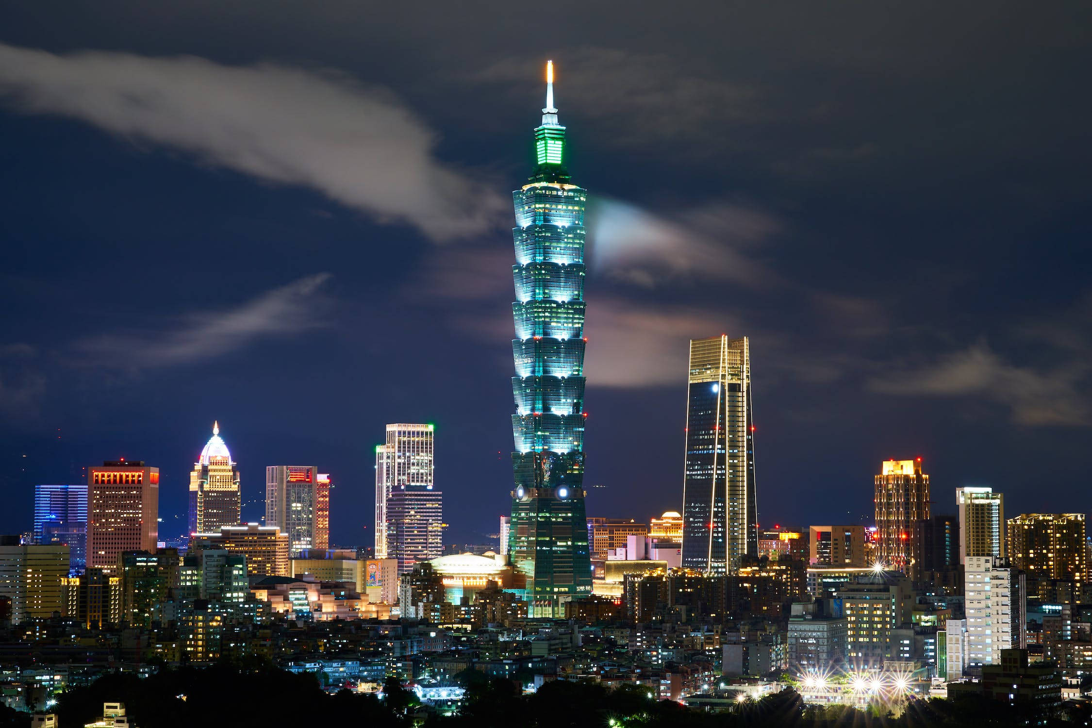 城市 桌布 壁紙 — 台北101摩天大樓在漆黑的夜空、散落的雲朵和周圍的城市燈光映襯下，呈現綠色照明。