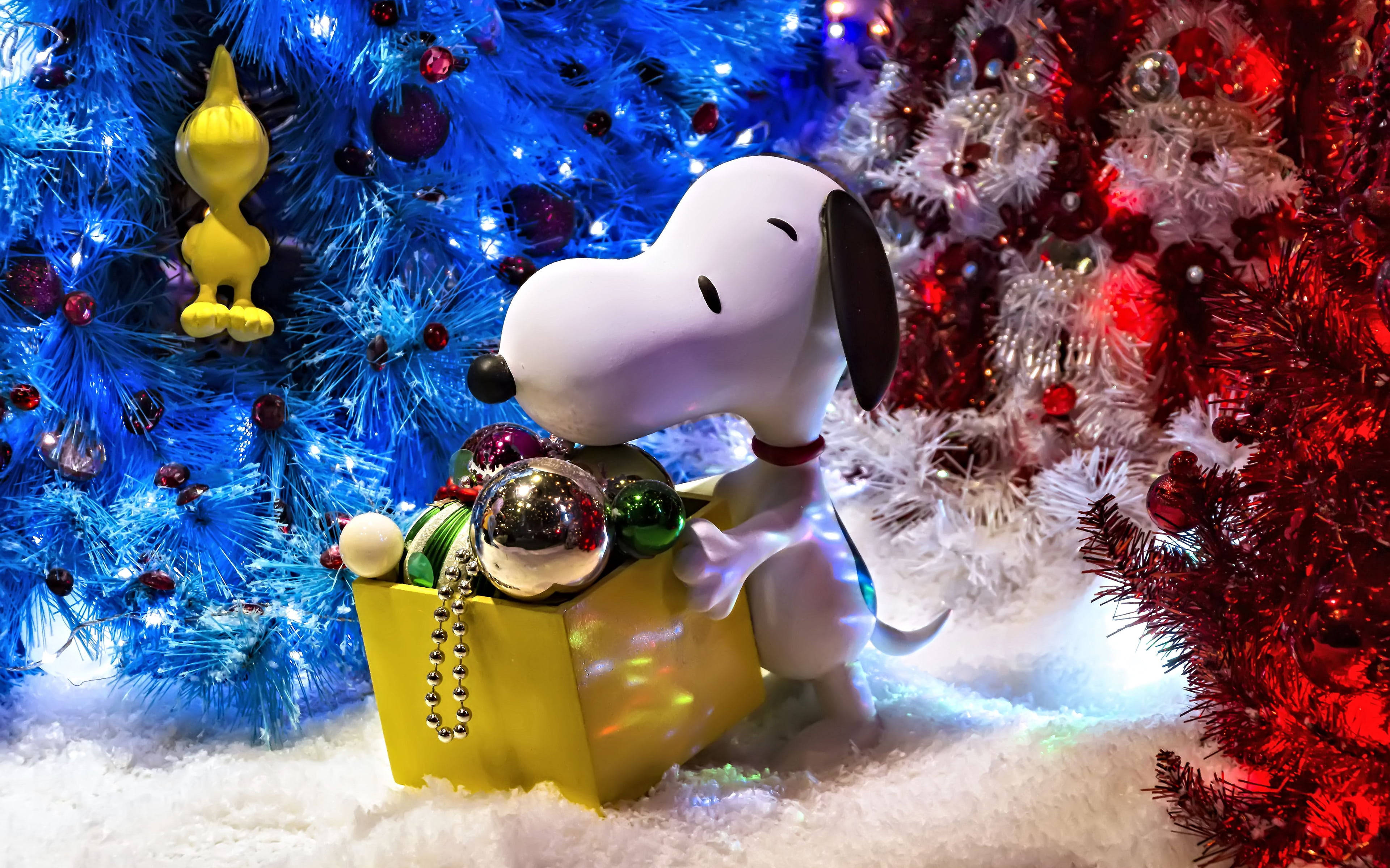 Snoopy Christmas 桌布 壁紙 — 史努比公仔依偎在雪中，旁邊是掛滿裝飾品和燈飾的藍色和紅色聖誕樹。