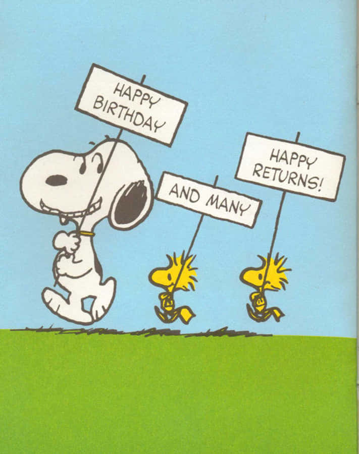 Charlie Brown Birthday 桌布 壁紙 — 史努比和兩隻糊士托在明亮的藍天和綠草背景下，高興地舉著寫有「Happy Birthday」和「Happy Returns!」的牌子。