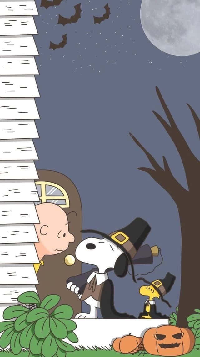 桌布 壁紙 — 史努比和查理布朗穿著萬聖節服裝，在滿月下從房子後面探出頭來，蝙蝠在頭頂飛翔。