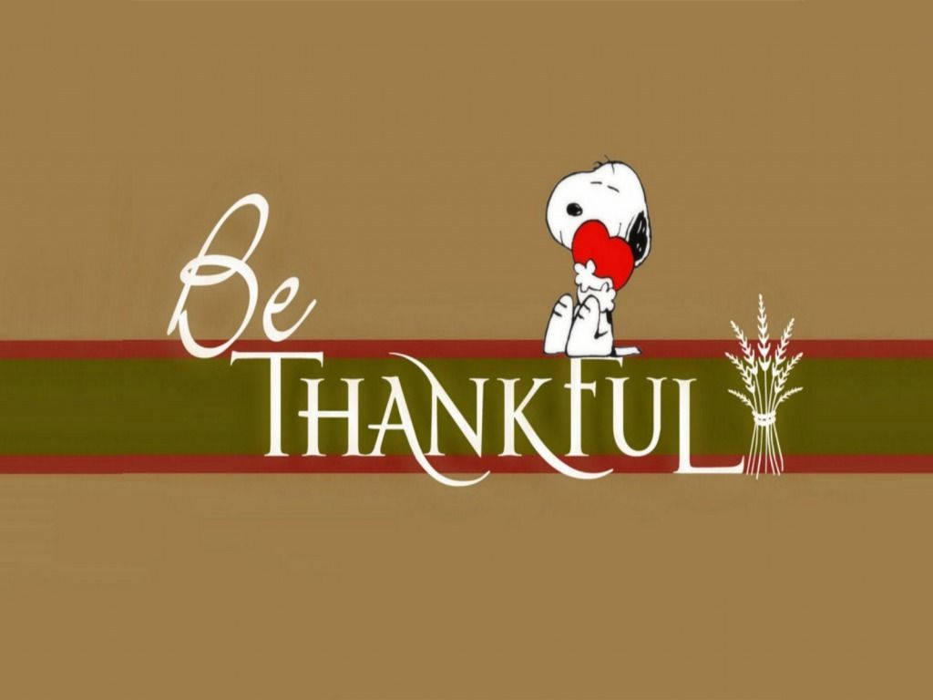 史努比拿著一個紅心，上面有「Be THANKFUL」文字和麥穗，背景是棕色。