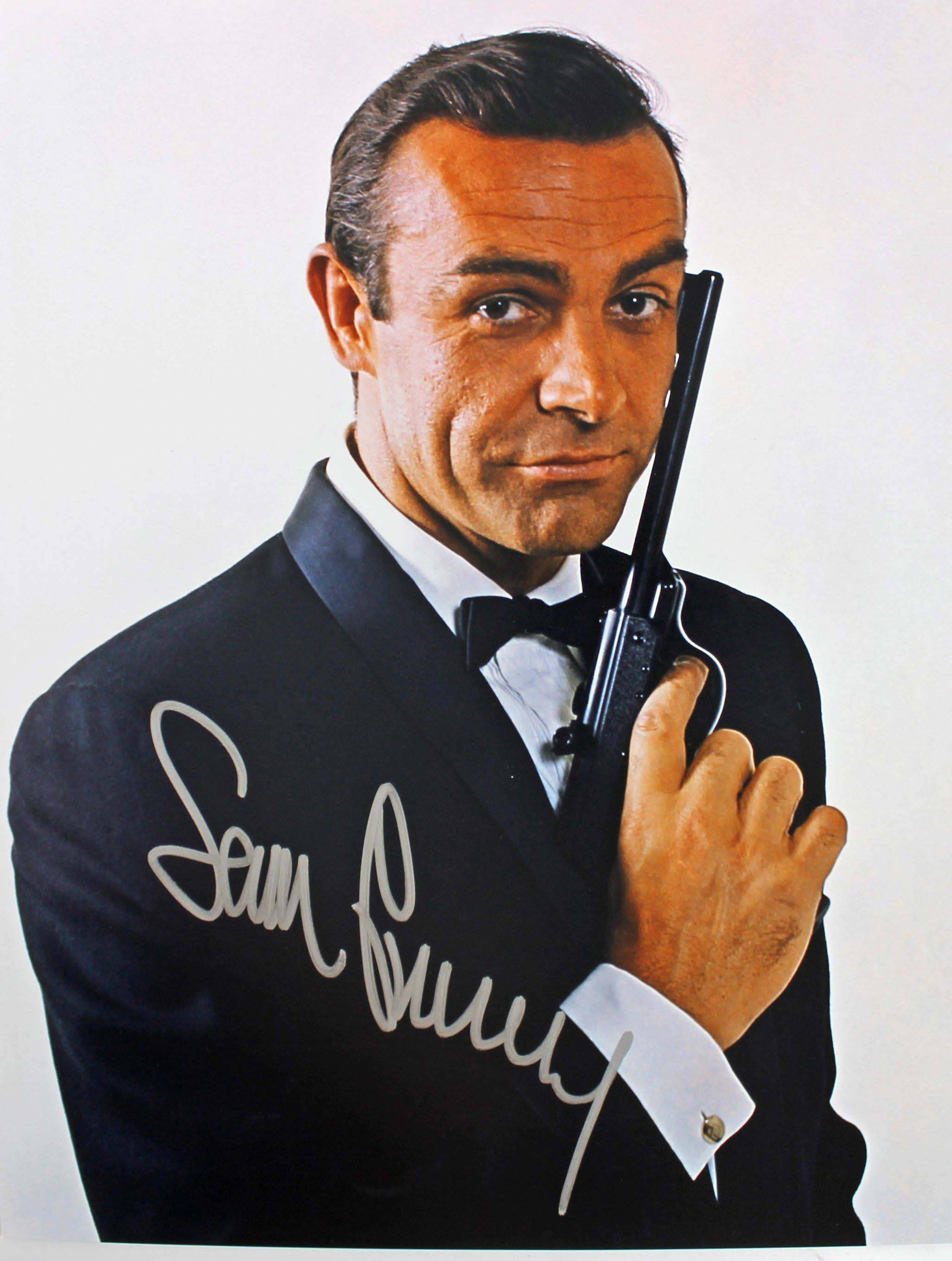 Sean Connery 桌布 壁紙 — 史恩·康納萊身穿禮服，手持手槍，自信微笑，背景為純白色。