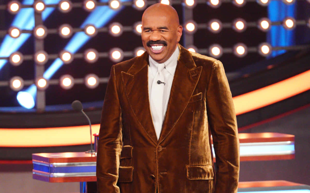 steve harvey 桌布 壁紙 — 史提夫·哈維穿著棕色天鵝絨西裝，在閃爍的舞台燈光和色彩繽紛的展板背景下閃耀登場。