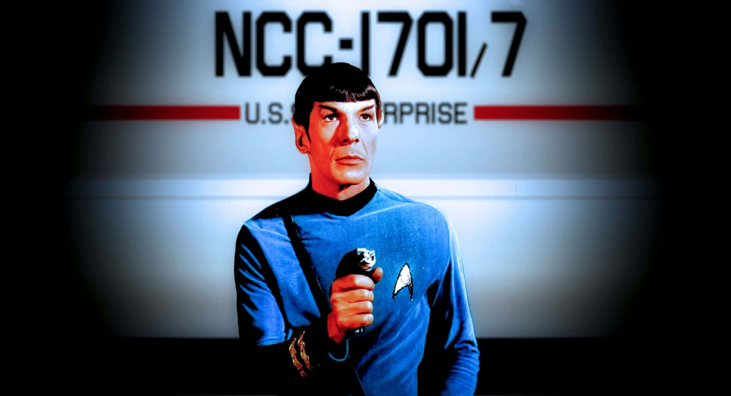 Spock 桌布 壁紙 — 史波克穿著藍色星際艦隊制服，手持通訊器，背景是模糊的飛船內部。