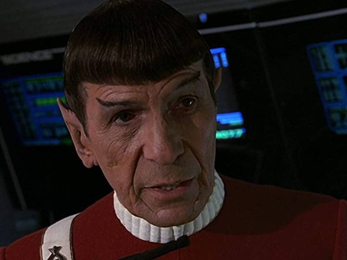 Spock 桌布 壁紙 — 史波克身穿紅色星際艦隊制服，擁有瓦肯耳朵和揚起的眉毛，背景是發光的藍色控制台螢幕的特寫。