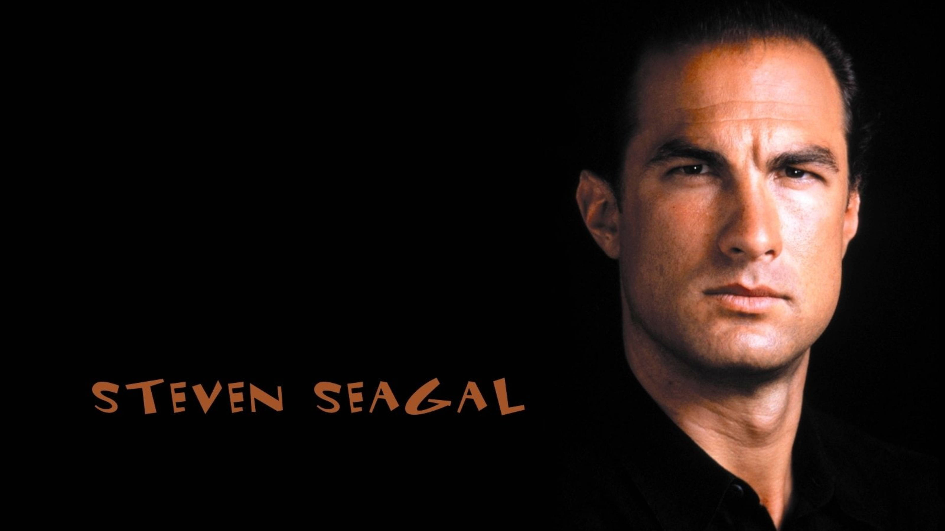 Steven Seagal 桌布 壁紙 — 史蒂芬·席格在黑色背景前凝視，他的名字以橙色文字顯示。