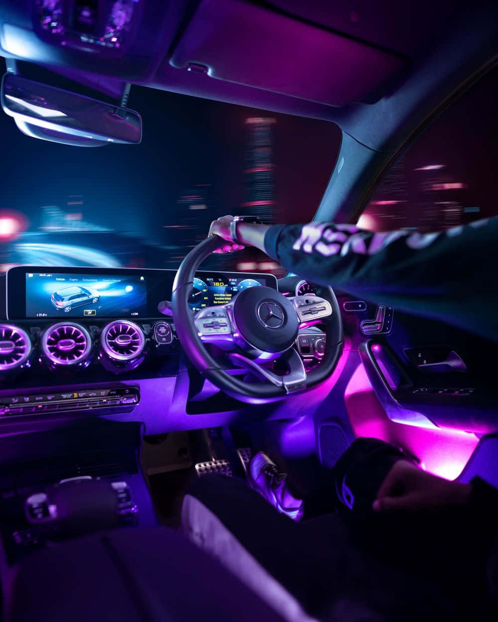 Inside Car 桌布 壁紙 — 司機在夜間抓著豪華車的方向盤，紫色環境燈照亮了高科技儀表板和外面模糊的城市景觀。