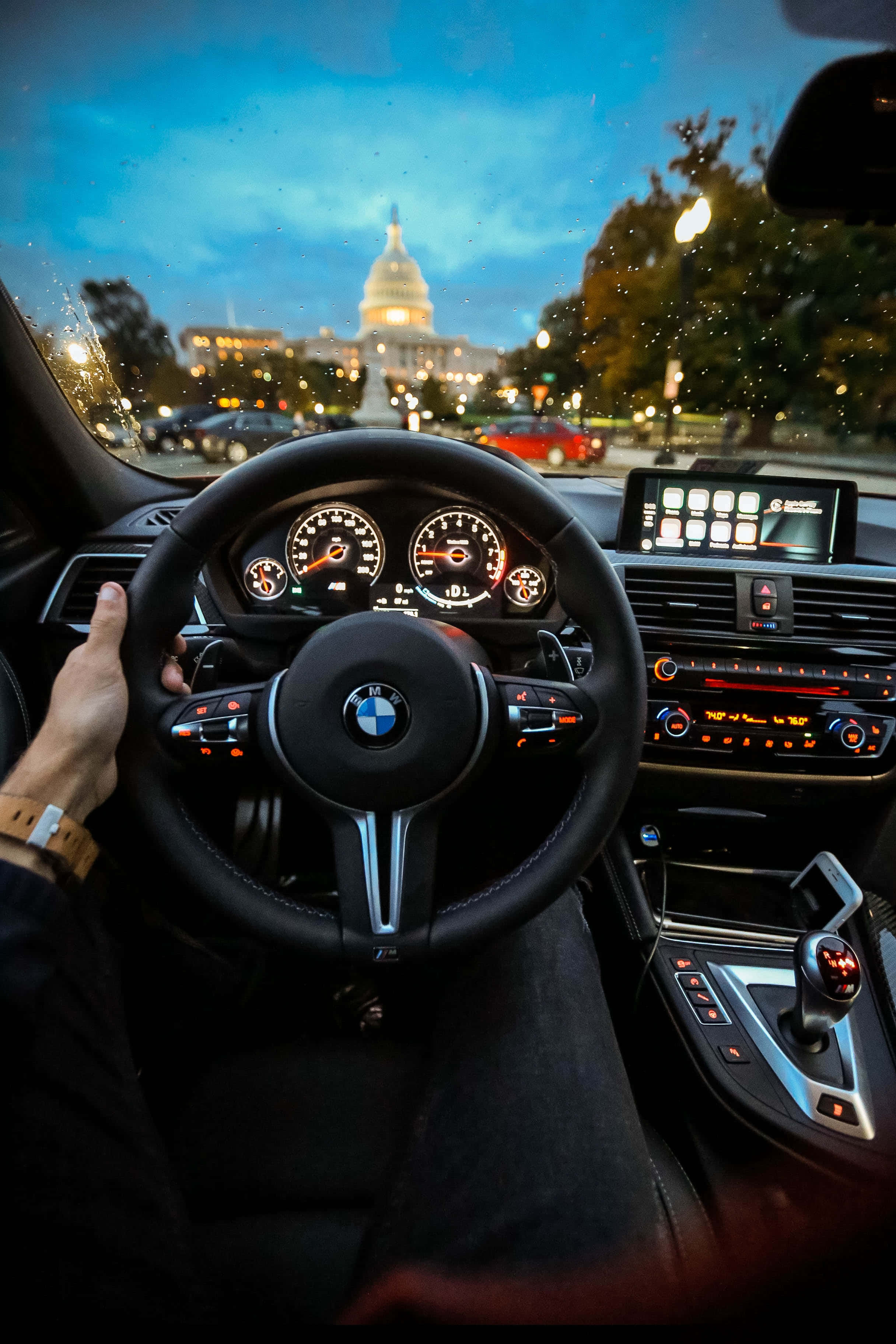 BMW 動圖 桌布 壁紙 — 司機的手握著BMW方向盤，國會大廈在暮色中透過擋風玻璃發光。