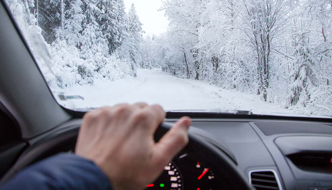 Winter Driving 桌布 壁紙 — 司機的手握著方向盤，一條積雪的森林道路蜿蜒向前，穿過冬季仙境。