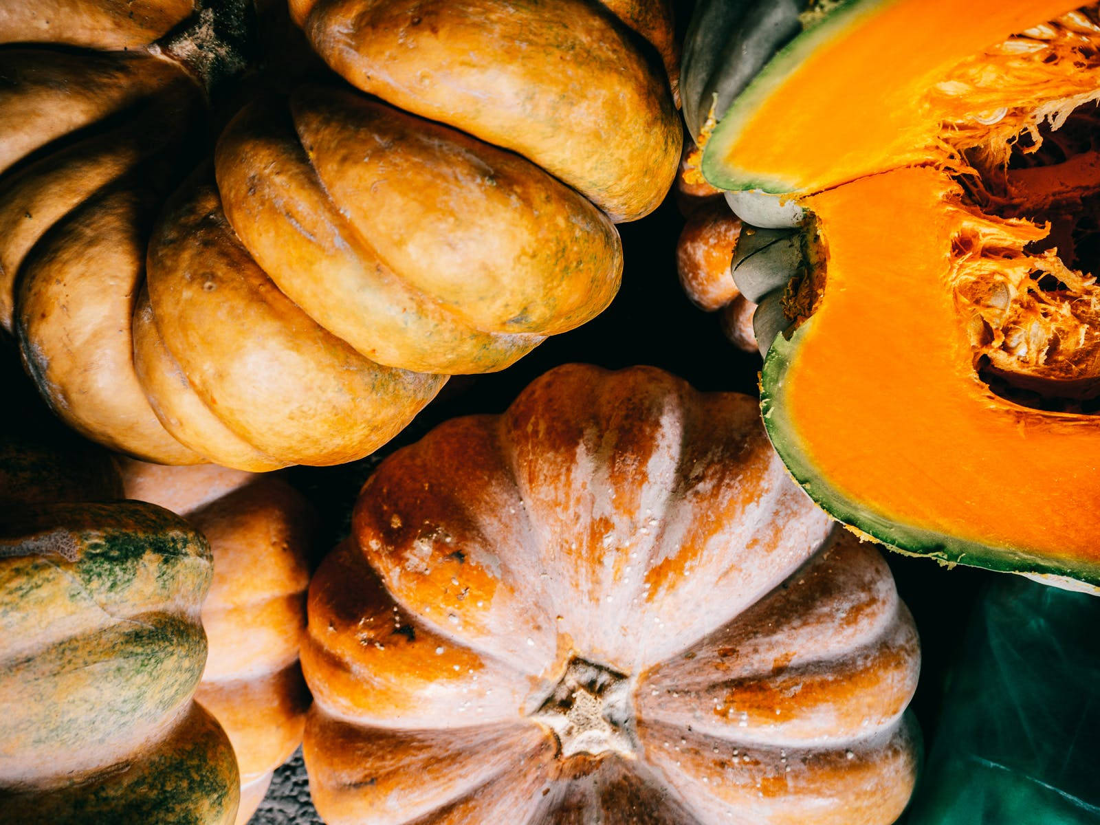 Rustic 桌布 壁紙 — 各種南瓜和 squash 的特寫，帶有豐富的橙色和綠色色調，展示紋理外皮和一個切半的南瓜，露出鮮豔的橙色果肉。