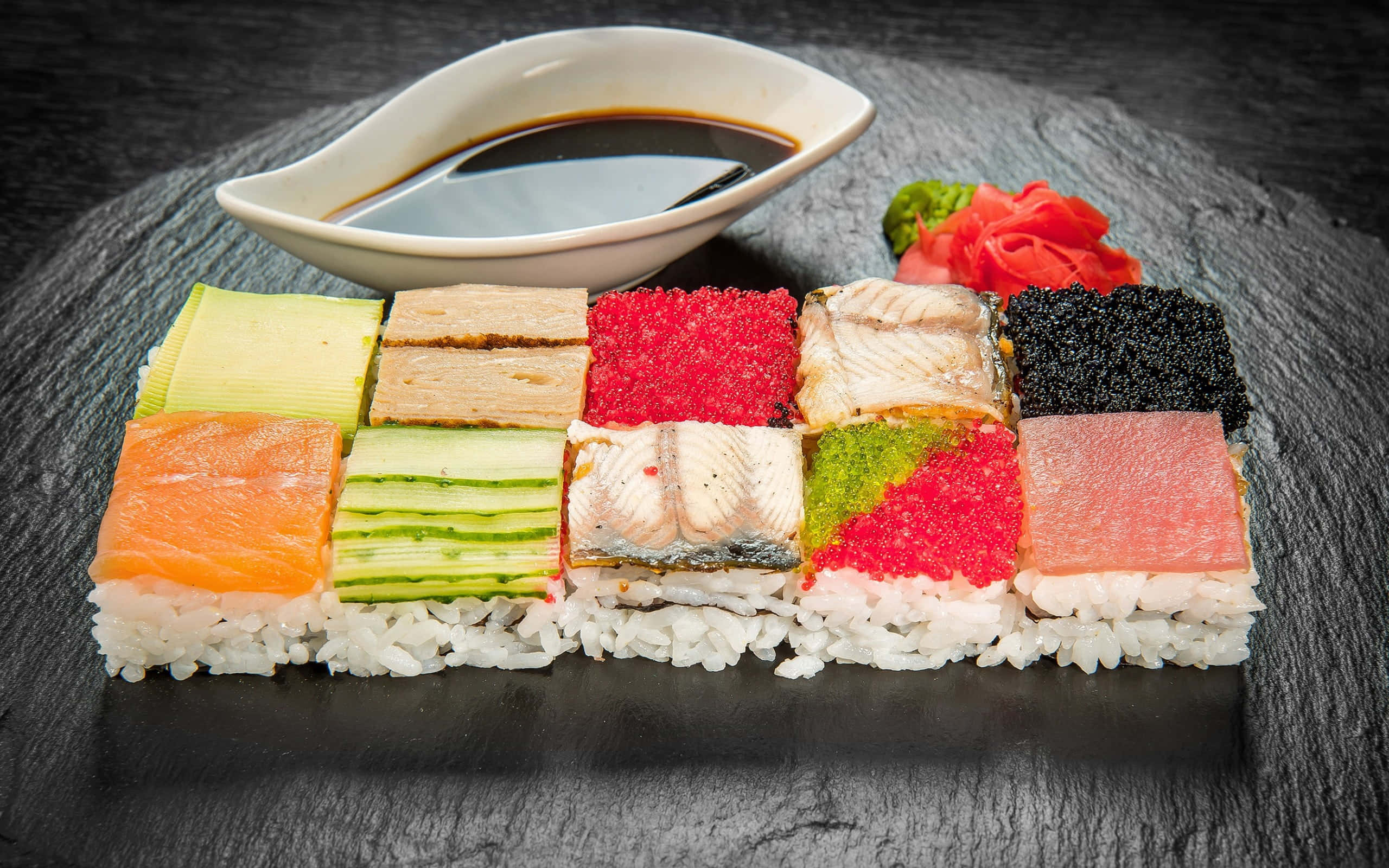 Food Photography 桌布 壁紙 — 各種壽司片色彩繽紛，整齊排列在深色石板盤上，搭配醬油和裝飾。