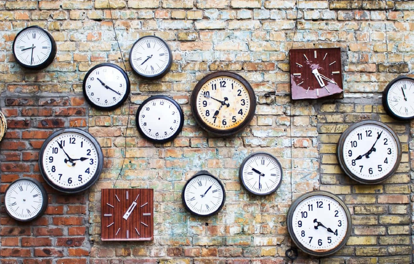 Clock 桌布 壁紙 — 各種尺寸和風格的復古時鐘混亂地掛在風化的磚牆上，每個顯示不同的時間。