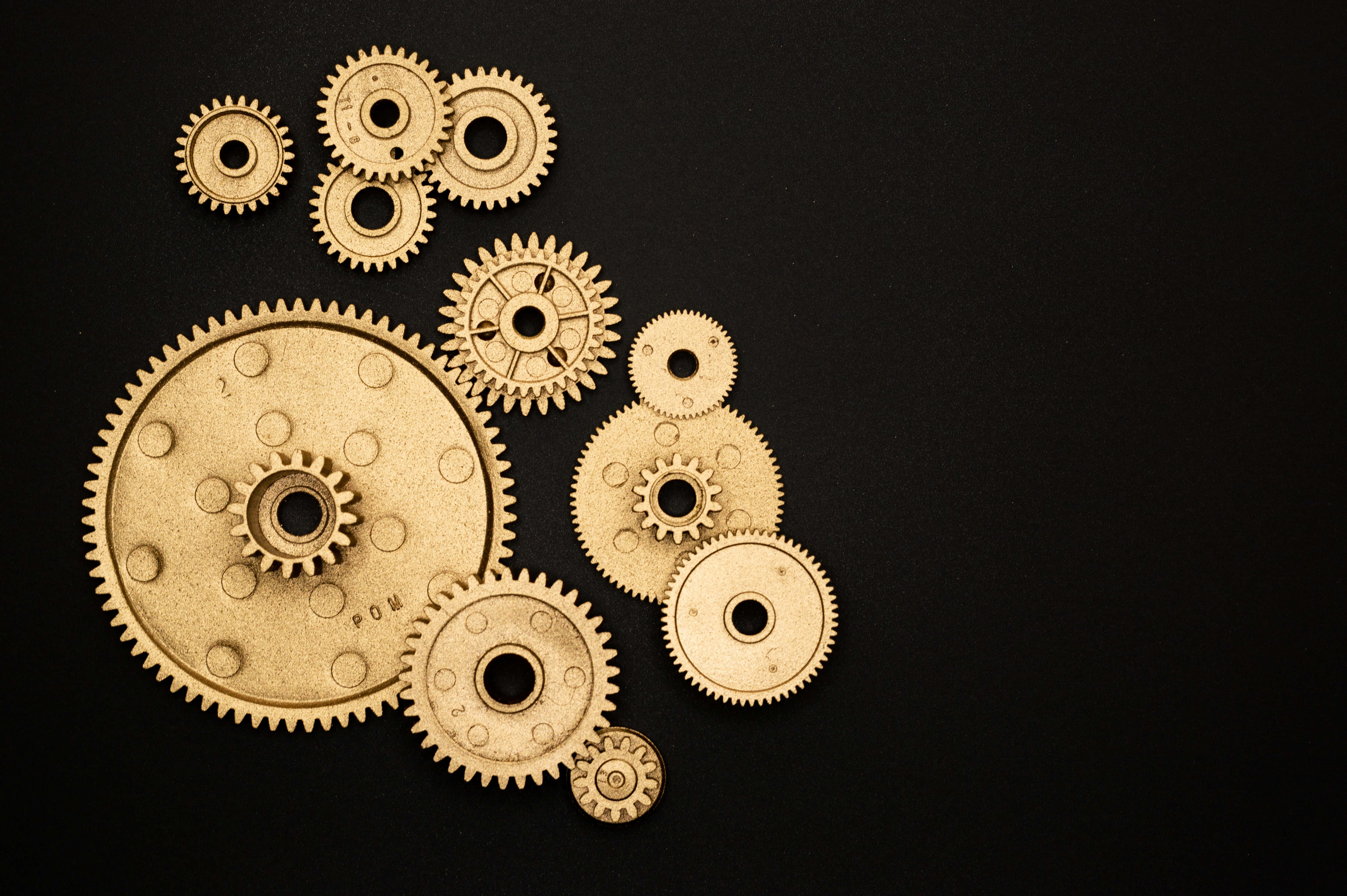 Mechanical Engineering 桌布 壁紙 — 各種尺寸的金色齒輪排列在黑色背景上，柔和的光線突顯其金屬質感。