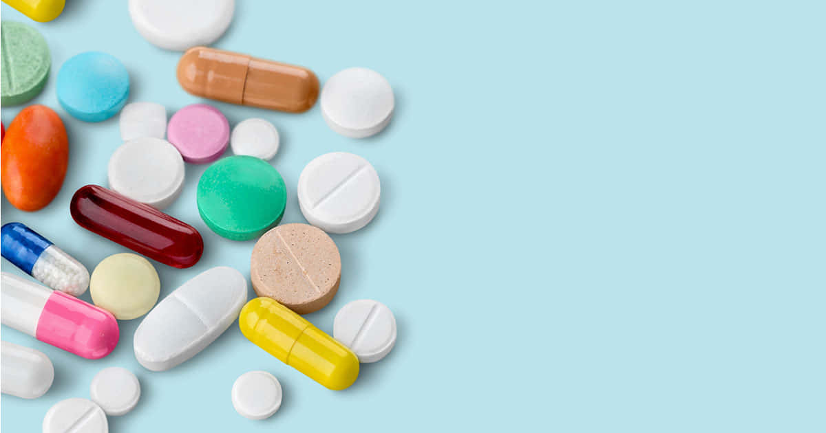 pills 桌布 壁紙 — 各種彩色藥丸和膠囊在柔和的藍色背景上對角散落。