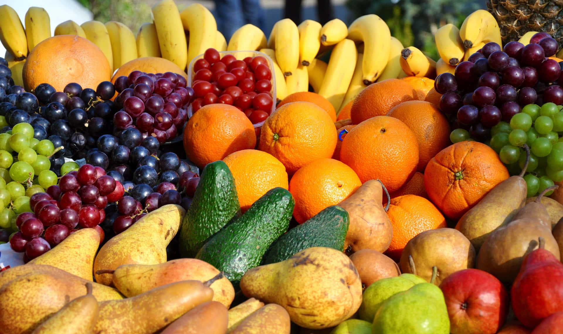 Winter Fruits 桌布 壁紙 — 各種新鮮水果包括香蕉、葡萄、柳橙、梨子和酪梨，以色彩繽紛、豐富的堆疊方式排列的鮮豔特寫。