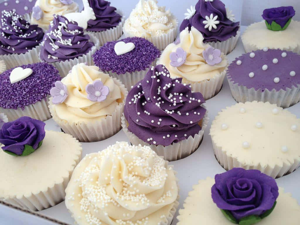 Cute Cupcake 桌布 壁紙 — 各種杯子蛋糕的特寫，帶有紫色和奶油色糖霜，裝飾著花朵糖粒和可食用玫瑰。
