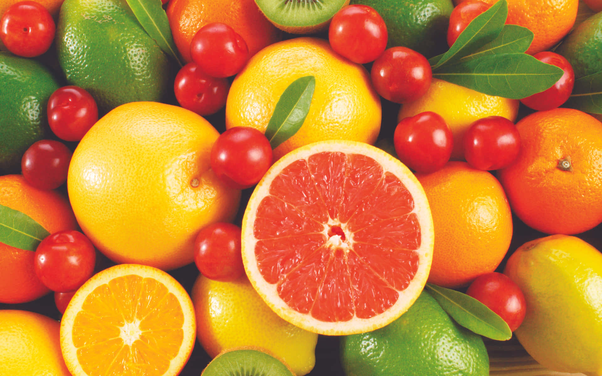 Fruits 桌布 壁紙 — 各種柑橘類水果的鮮豔特寫，包括葡萄柚、柳橙、檸檬和櫻桃番茄，搭配綠葉。