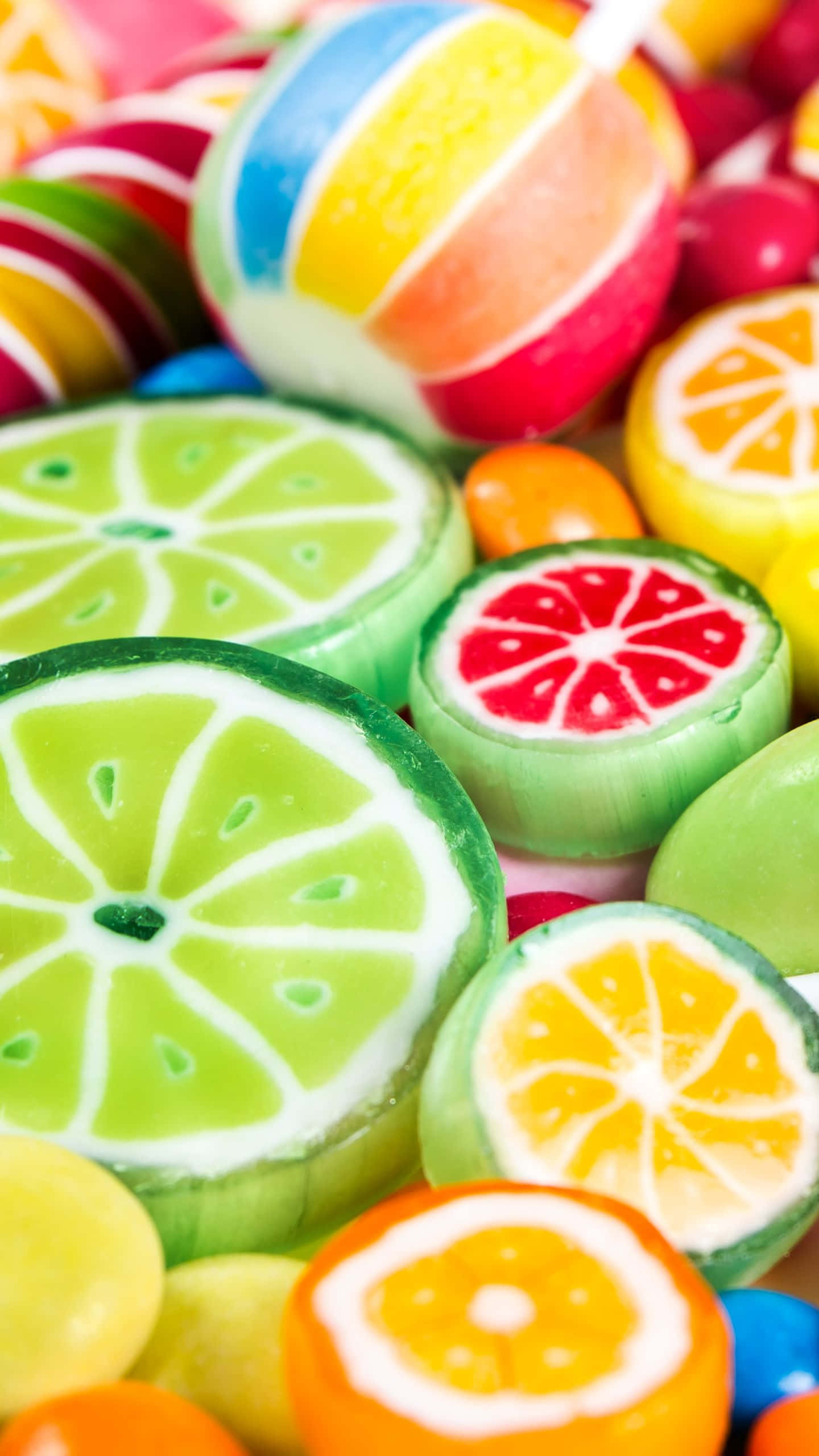糖果 桌布 壁紙 — 各種柑橘類糖果的特寫，形狀像萊姆、橙子和葡萄柚片，搭配色彩繽紛的條紋棒棒糖。