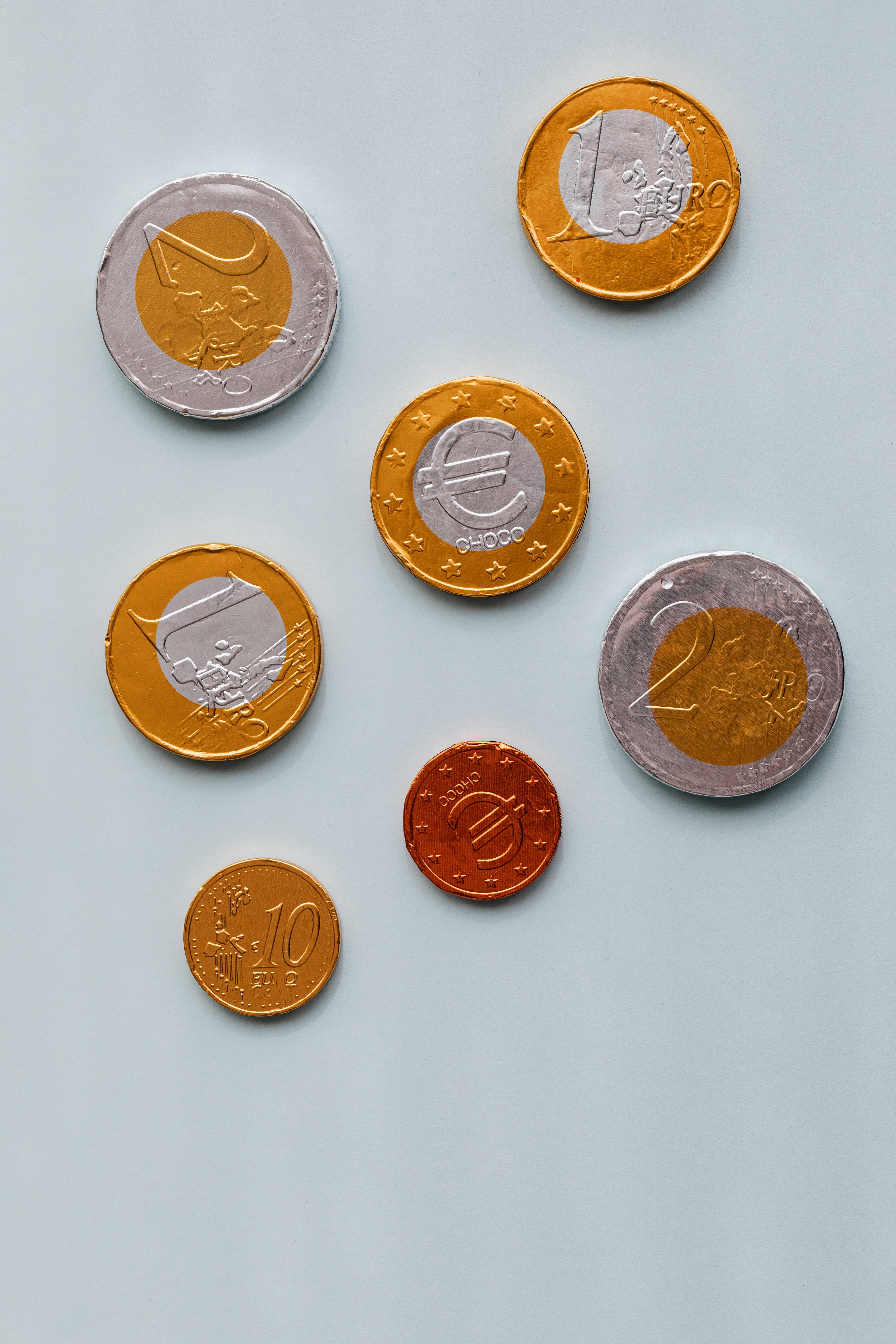 金錢 桌布 壁紙 — 各種歐元硬幣散落在純淺灰色表面上，顯示不同的面額和金屬飾面。