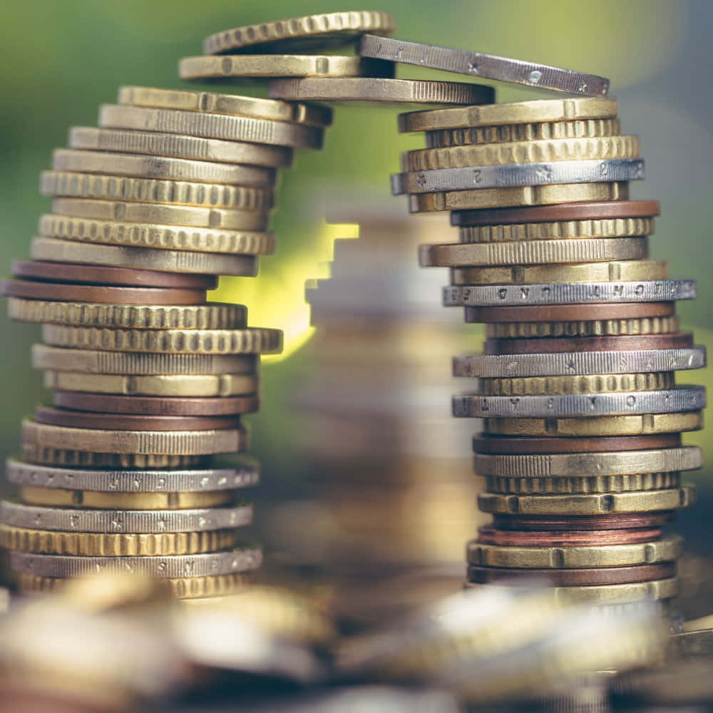 Coin 桌布 壁紙 — 各種硬幣堆疊成拱形，框住一道在柔和綠色背景上發光的光線。