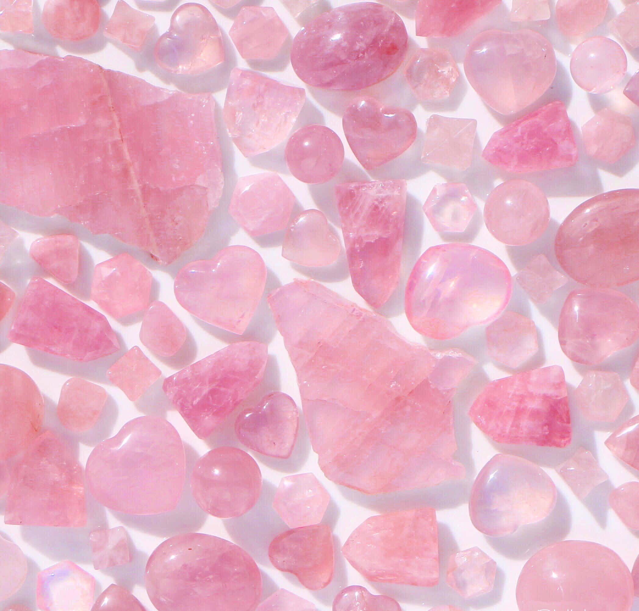 Pink Crystal Quartz 桌布 壁紙 — 各種粉紅玫瑰石英晶體和心形石頭散落在亮白色表面上的特寫。