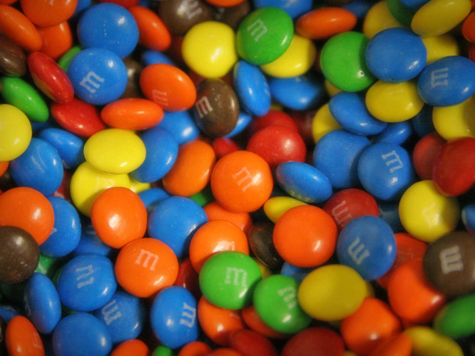 Chocolate 桌布 壁紙 — 各種色彩繽紛的M&M's糖果的鮮明特寫，帶有光澤外殼和白色「m」標誌。