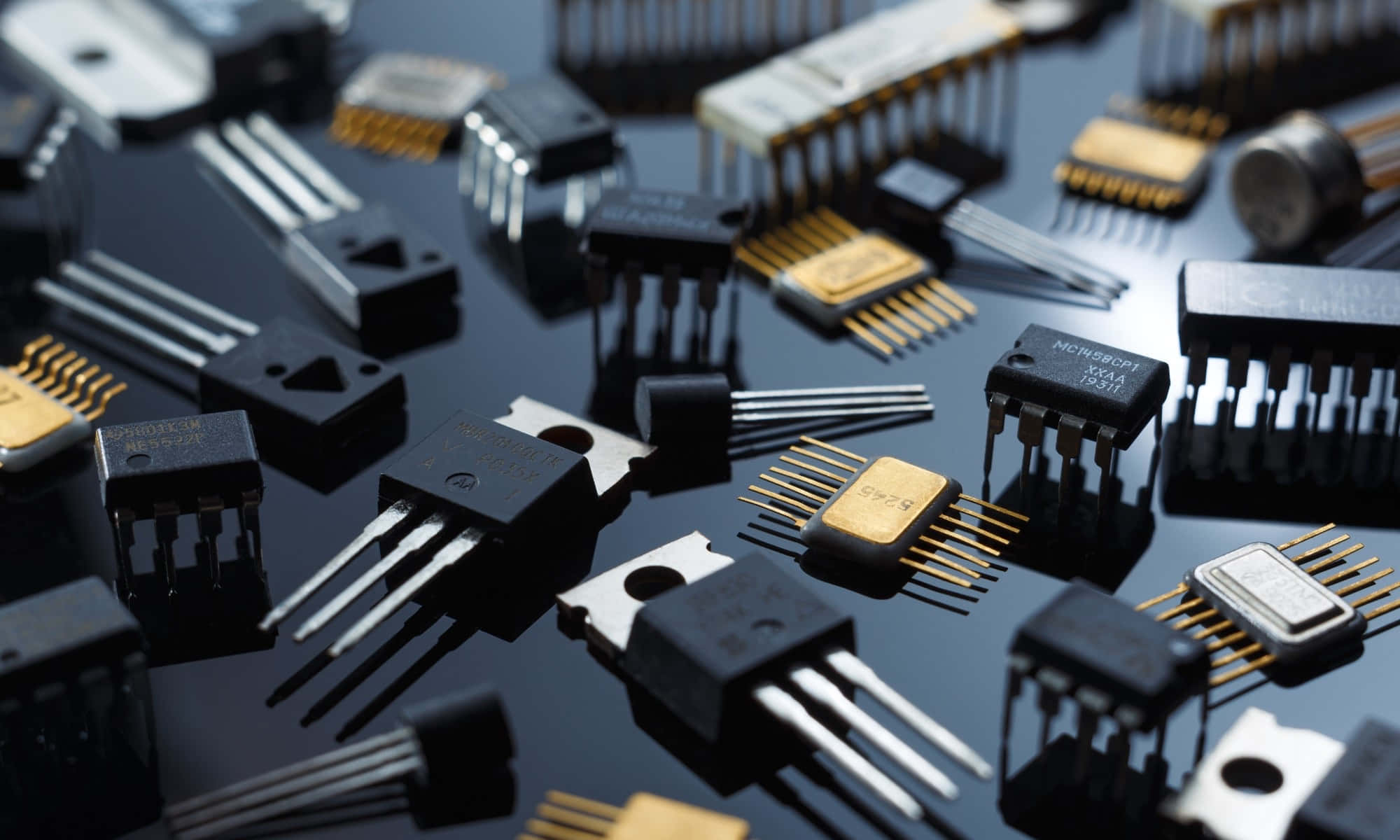 Electronic Components 桌布 壁紙 — 各種電子元件（如電晶體和積體電路）散落在反光黑色表面上的特寫。