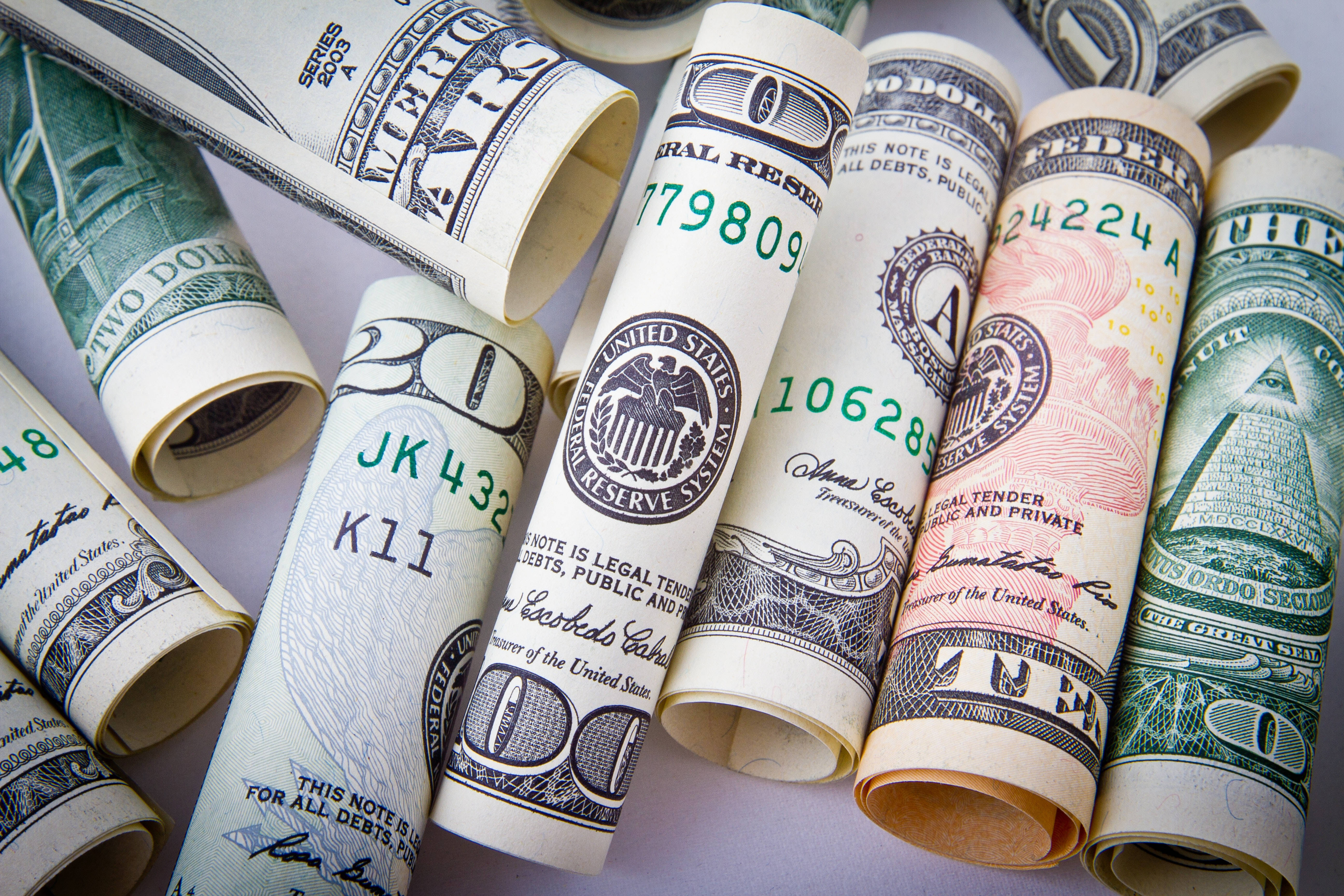 金錢 桌布 壁紙 — 各種面額的捲起美元鈔票散落在淺色表面上。