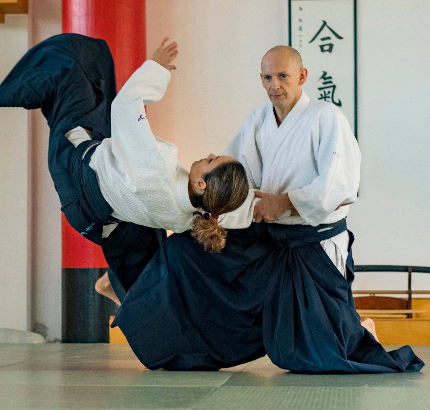 martial arts 桌布 壁紙 — 合氣道練習者在傳統道場的墊子上執行一個動態的投擲，牆上有書法。