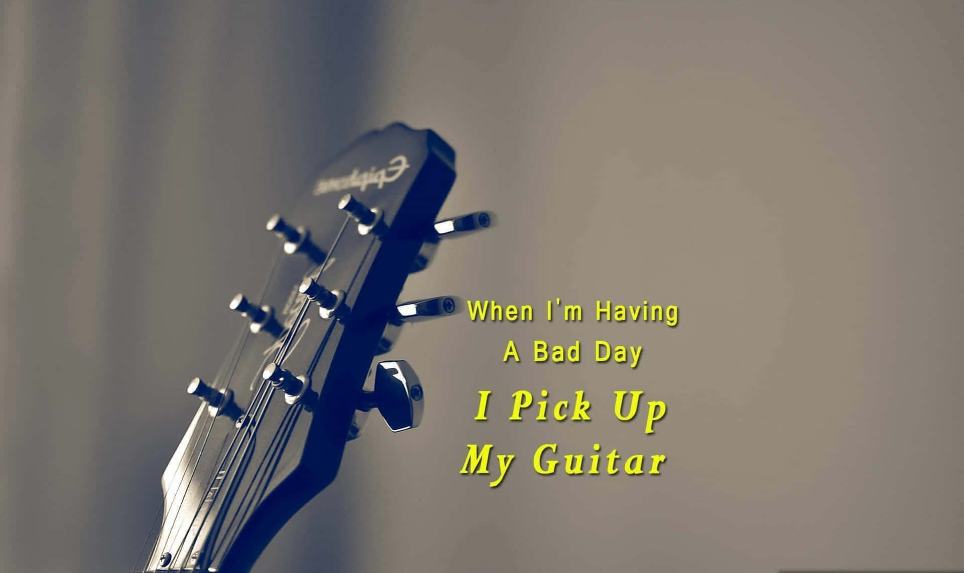 語錄 桌布 壁紙 — 吉他頭部特寫，帶有文字疊加 'When I'm Having A Bad Day I Pick Up My Guitar'，背景柔和模糊。