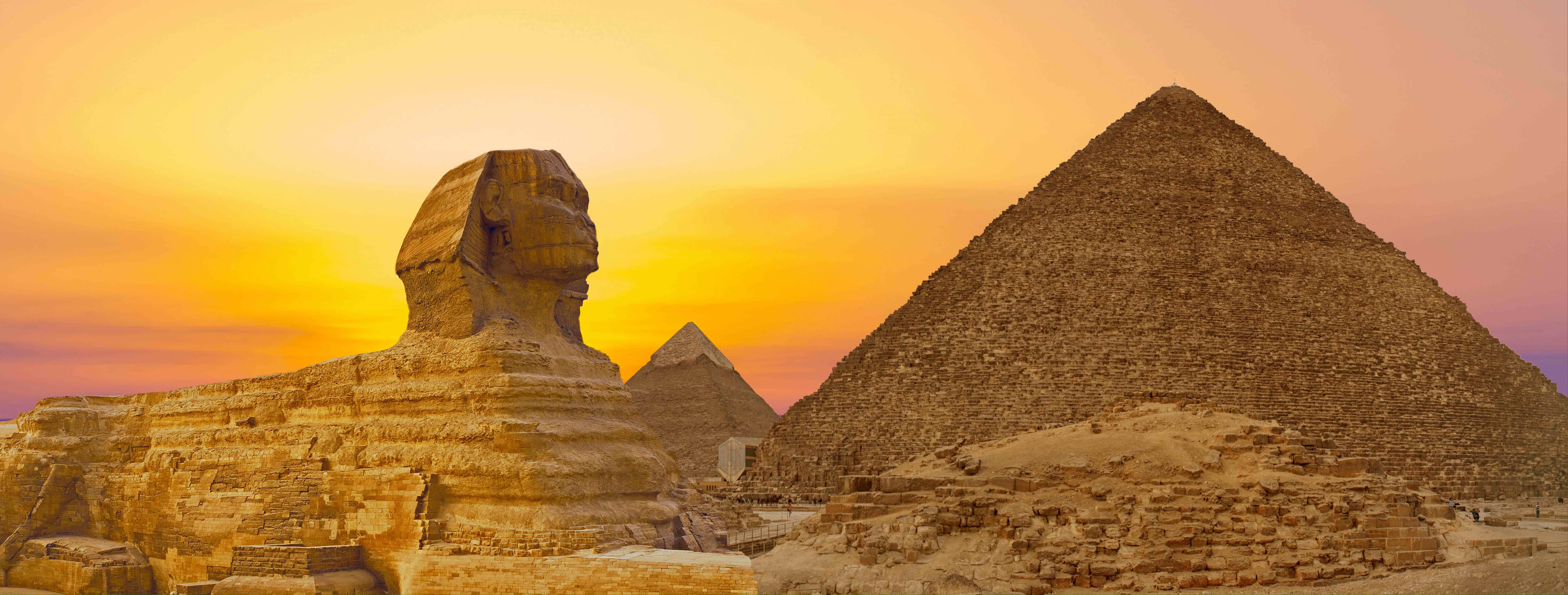 Ancient Egypt 桌布 壁紙 — 吉薩大獅身人面像和金字塔在熾熱的夕陽天空下，以溫暖的金色色調巍然聳立。