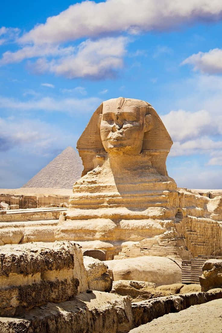 pyramid 桌布 壁紙 — 吉薩大獅身人面像在明亮的藍天下雄偉地矗立，背景中可見金字塔和散落的雲朵。