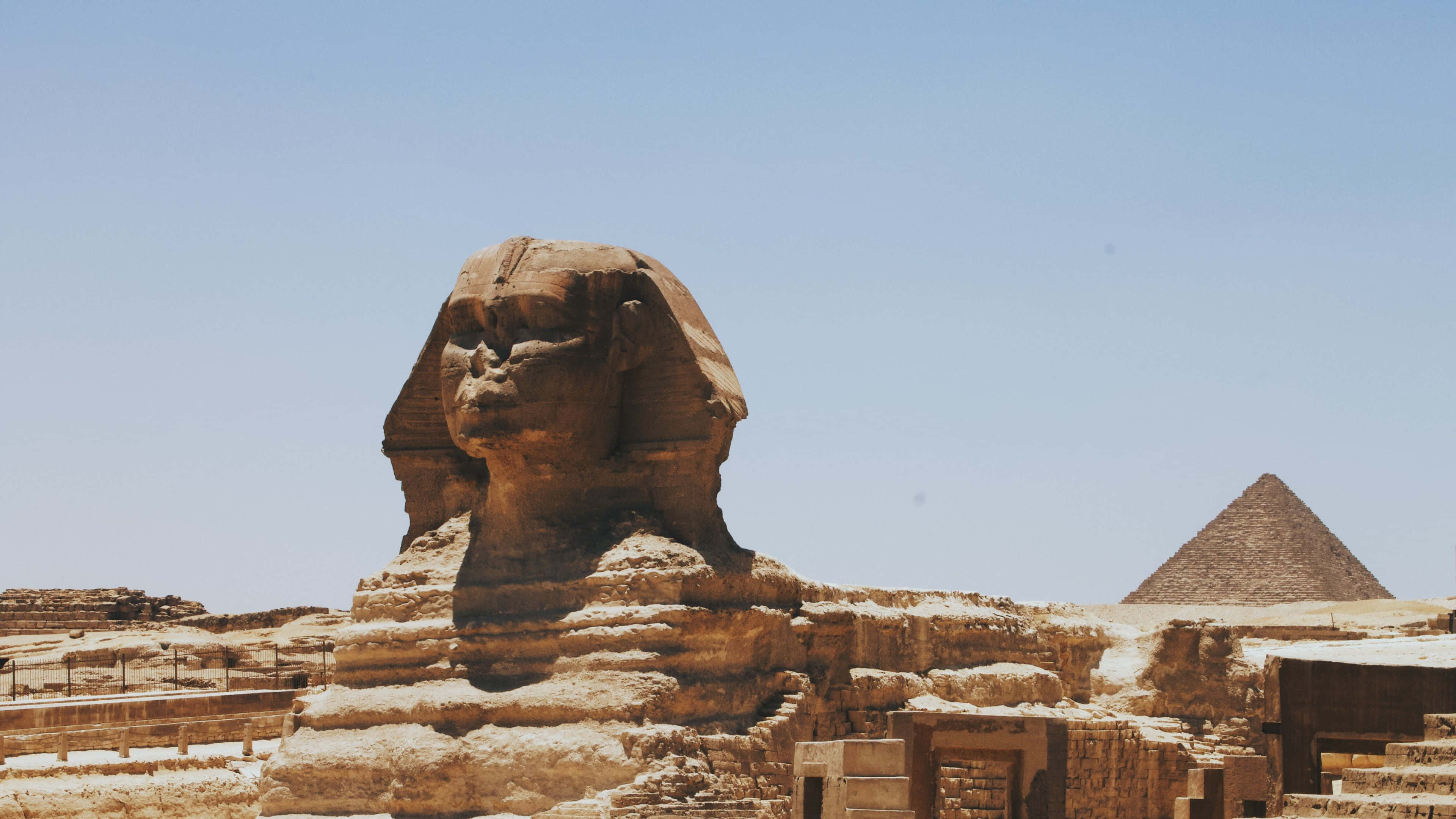 Ancient Egypt 桌布 壁紙 — 吉薩大獅身人面像在晴朗的藍天下雄偉地矗立，遠處可見金字塔。