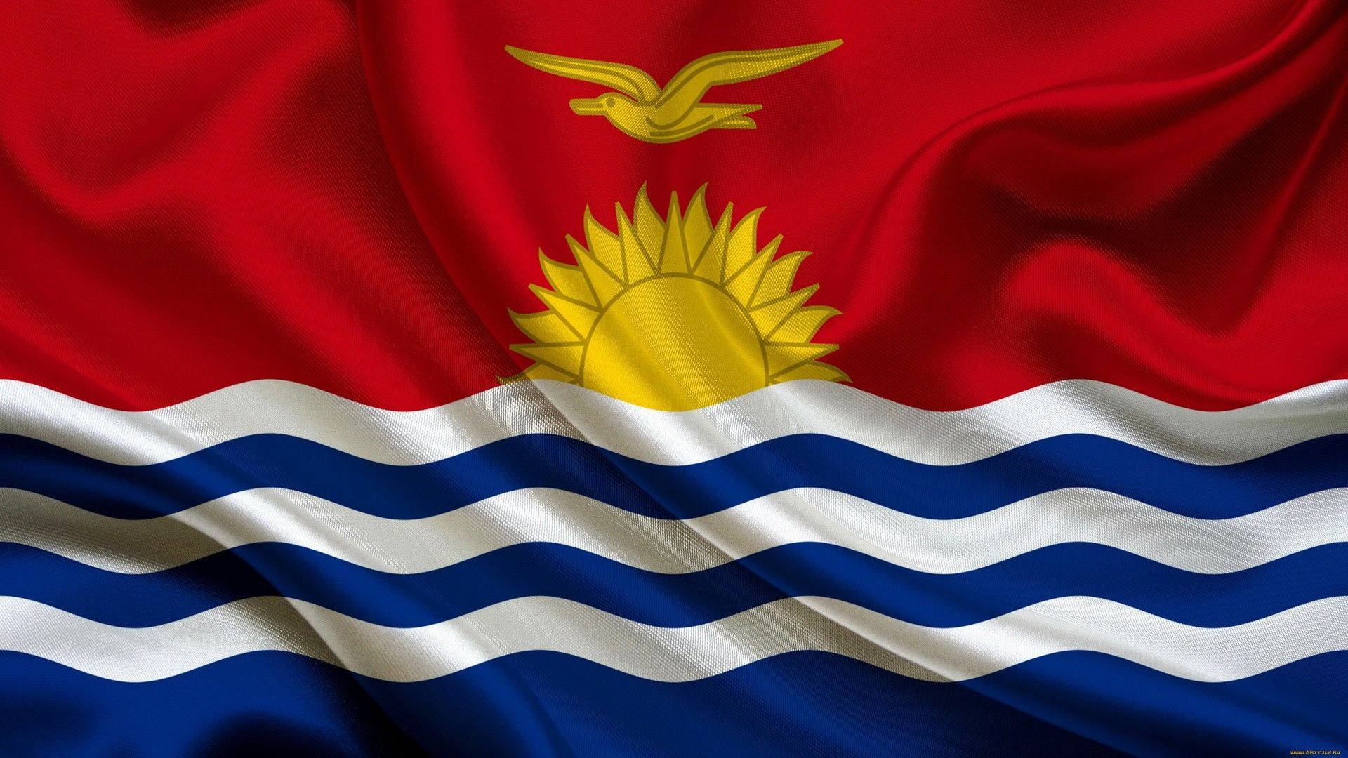 Kiribati 桌布 壁紙 — 吉里巴斯國旗動態飄揚，採用豐富的紅色布料、金色太陽和軍艦鳥，以及象徵太平洋的藍白波浪條紋。