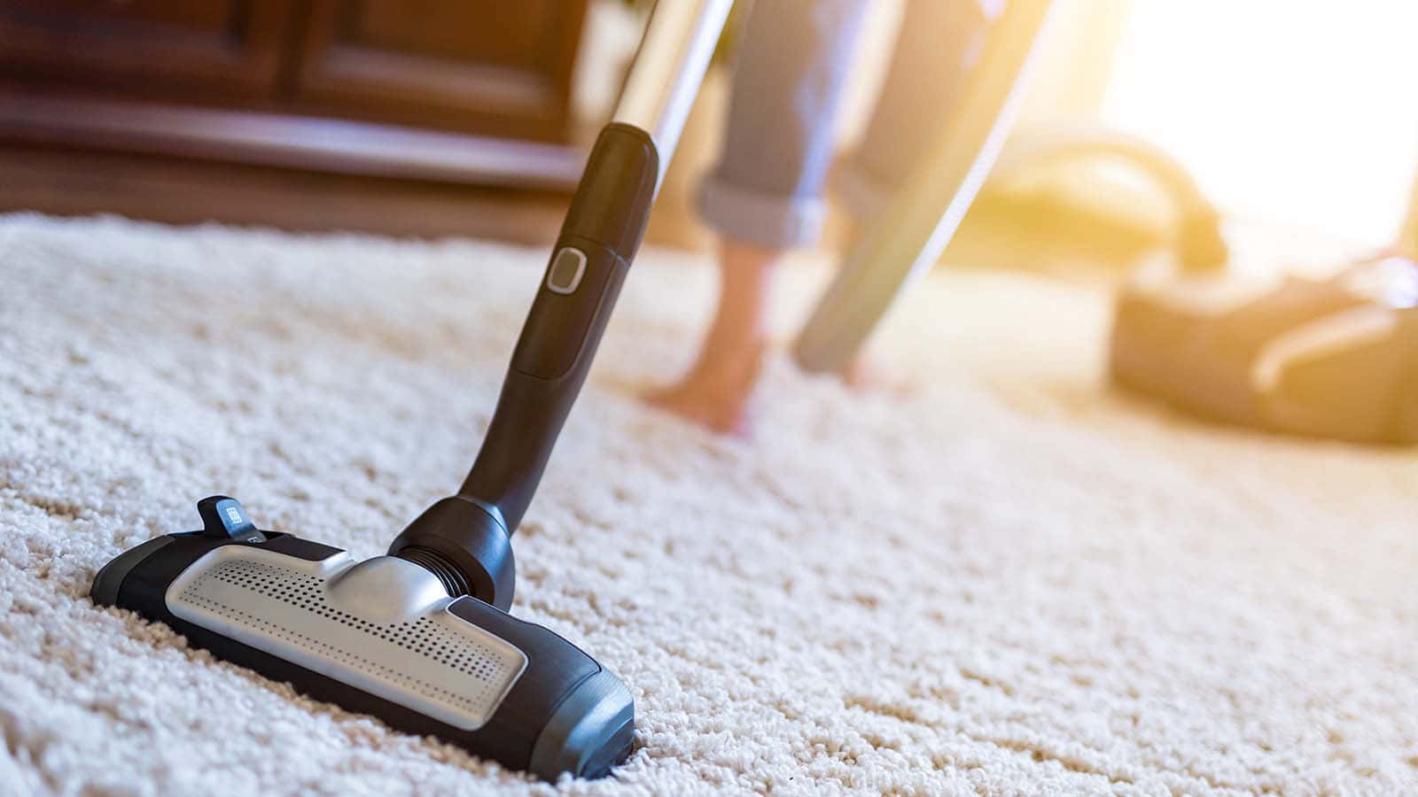 Cleaning 桌布 壁紙 — 吸塵器頭在柔軟的米色地毯上滑行的特寫，一個人在陽光充足的房間裡打掃。